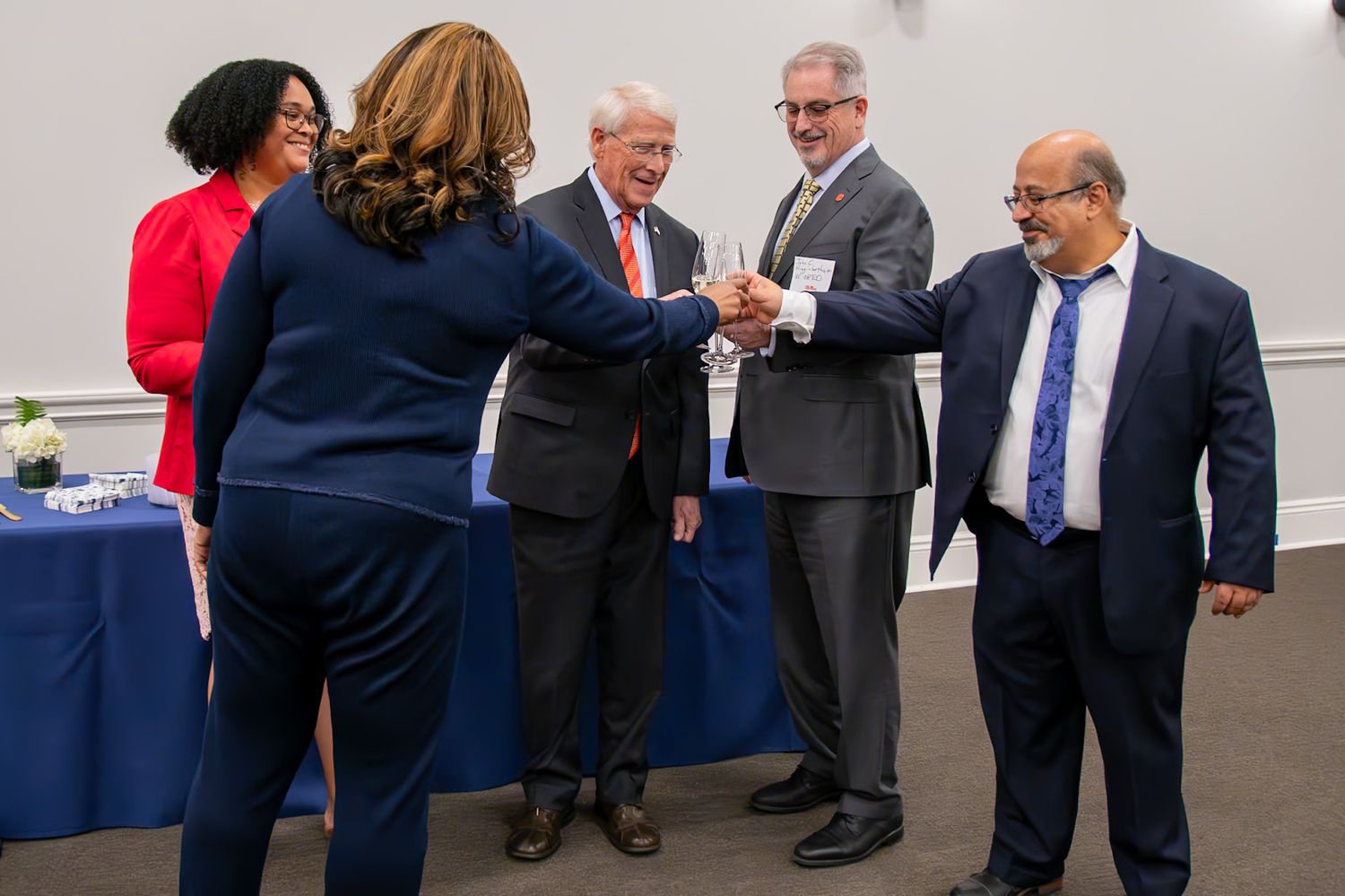Professionals in formal attire shaking hands at a business networking event in a conference room.
