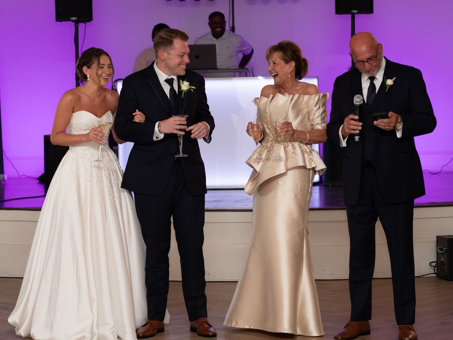 A formal event with four people in elegant attire holding drinks and toasting during a reception with purple lighting.