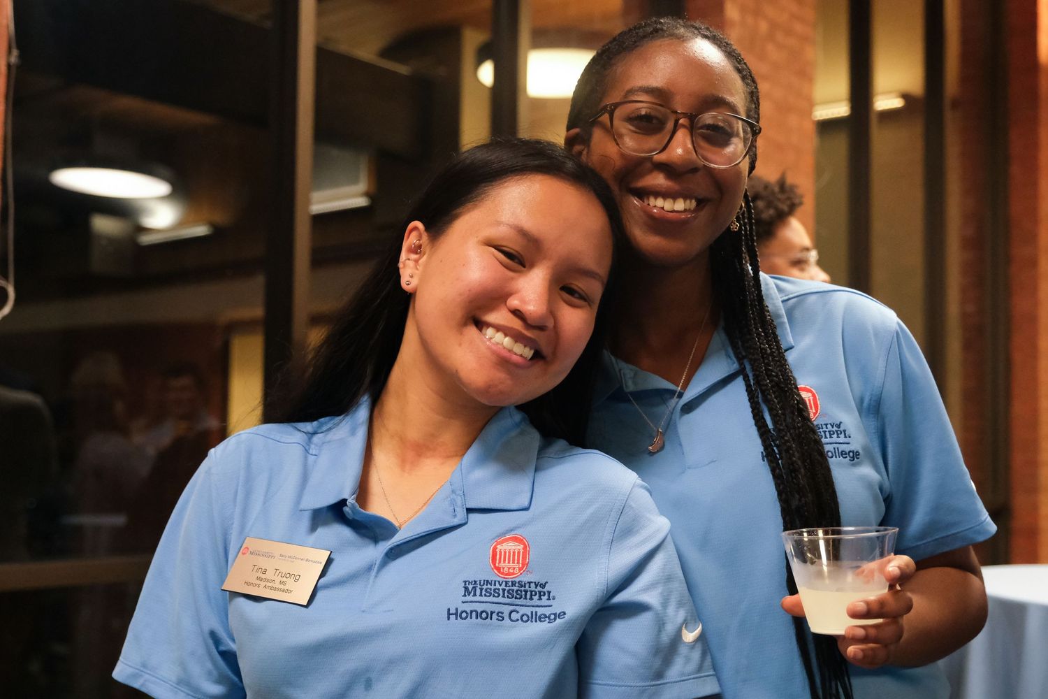 Two smiling young women in blue Harper College uniforms pose together at a campus event.