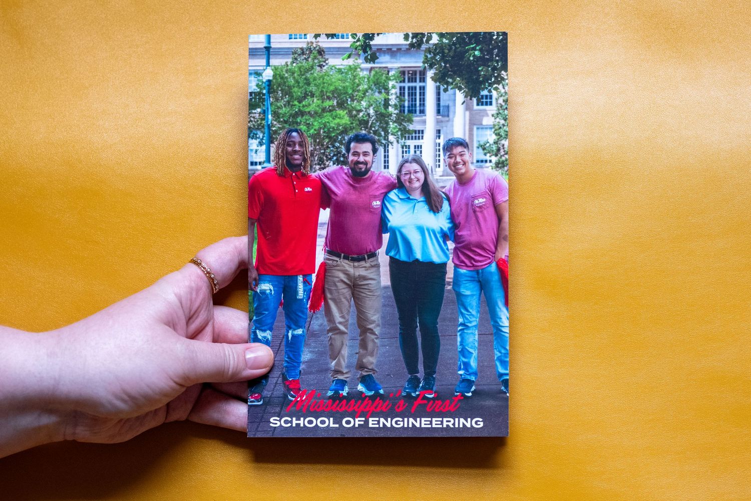 Hand holding a School of Engineering brochure featuring four smiling students posing outdoors on campus.