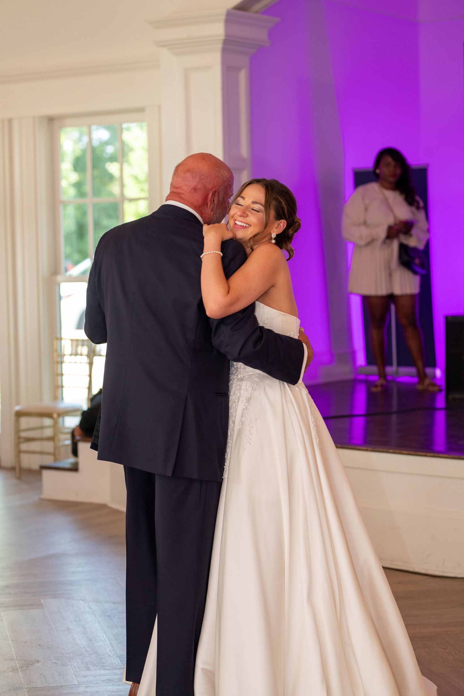 A couple shares an intimate dance together during a wedding reception in an elegant venue with purple lighting.