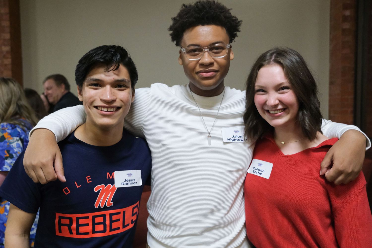 Three smiling college students wearing Ole Miss Rebels shirts pose together at a campus social event.