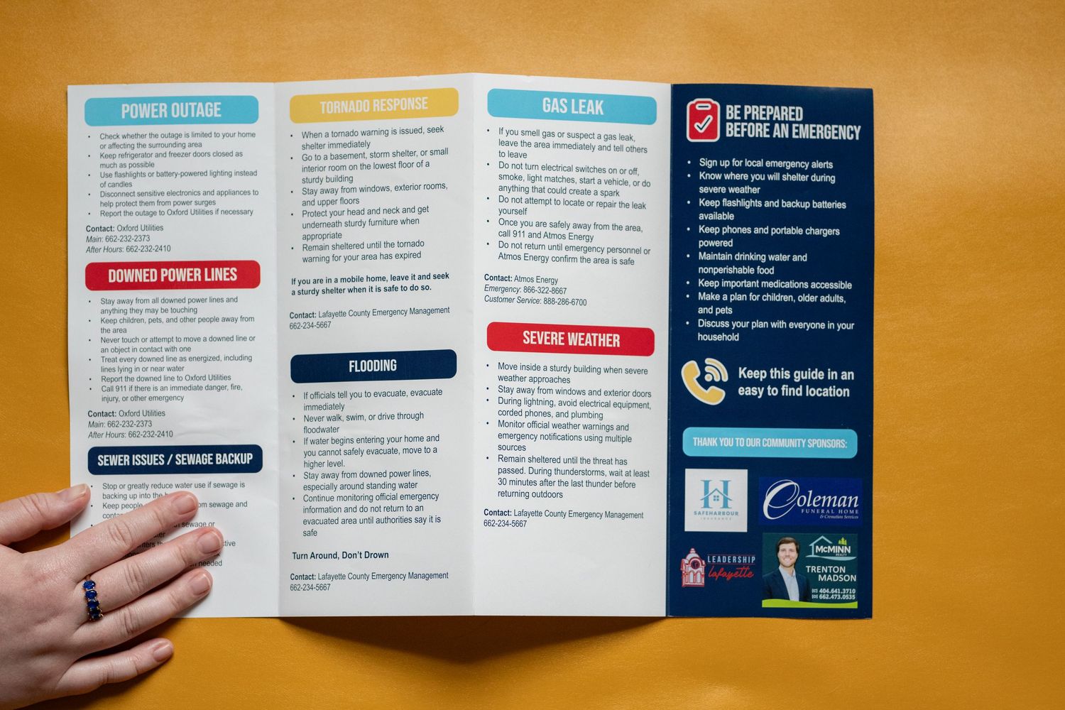Hand holding an open emergency preparedness brochure with sections on power outages, flooding, and severe weather tips.