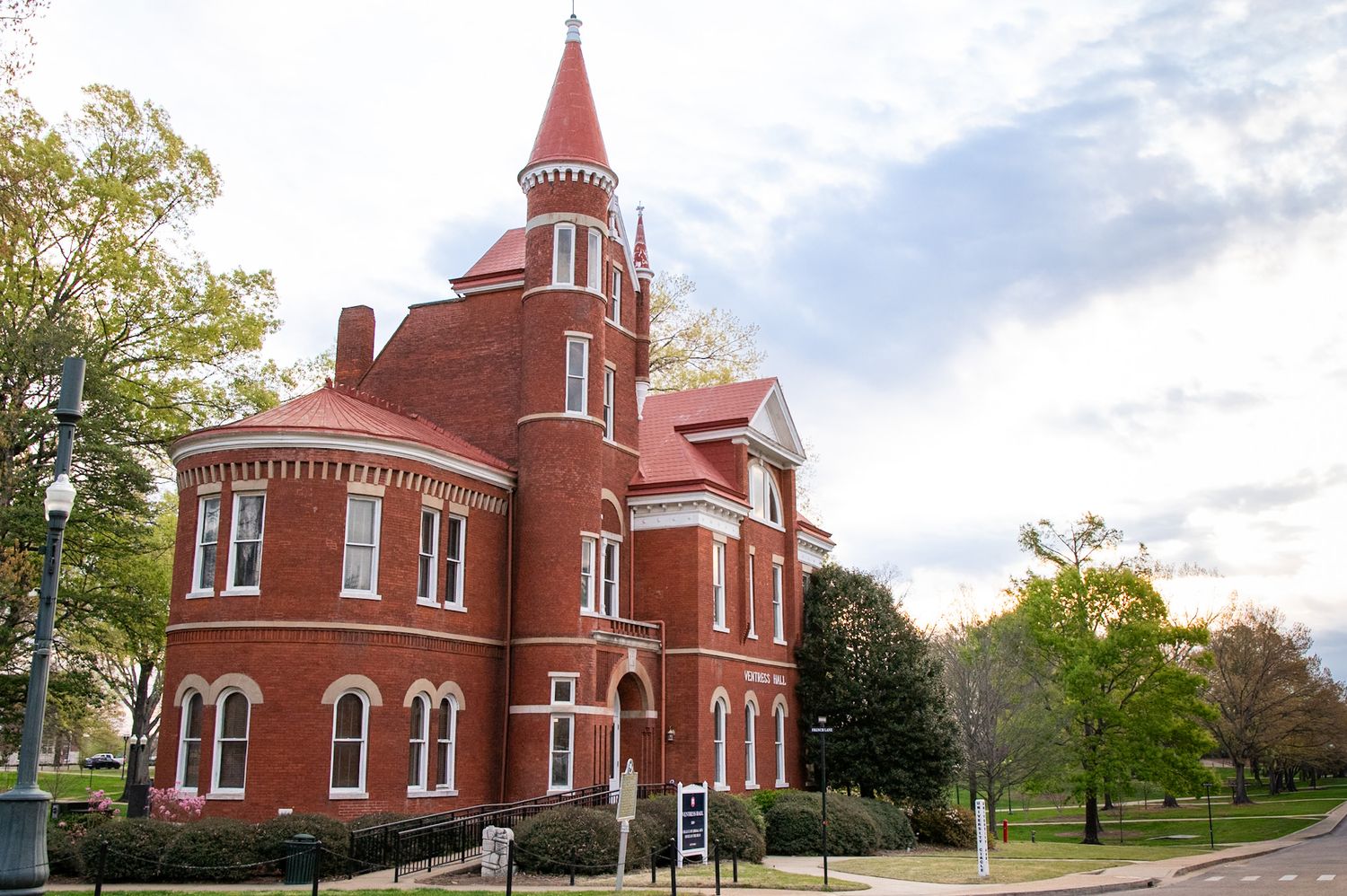 Historic red brick Victorian building with turret on a college campus surrounded by green trees.