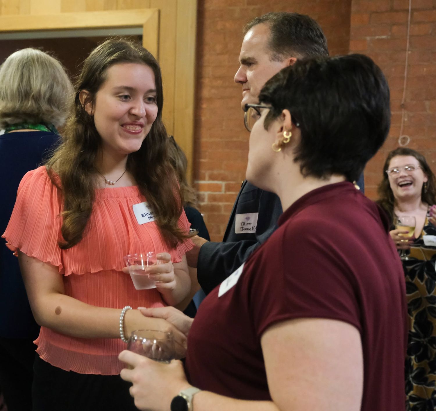 People networking at a social gathering, smiling and conversing in a warmly lit indoor venue.