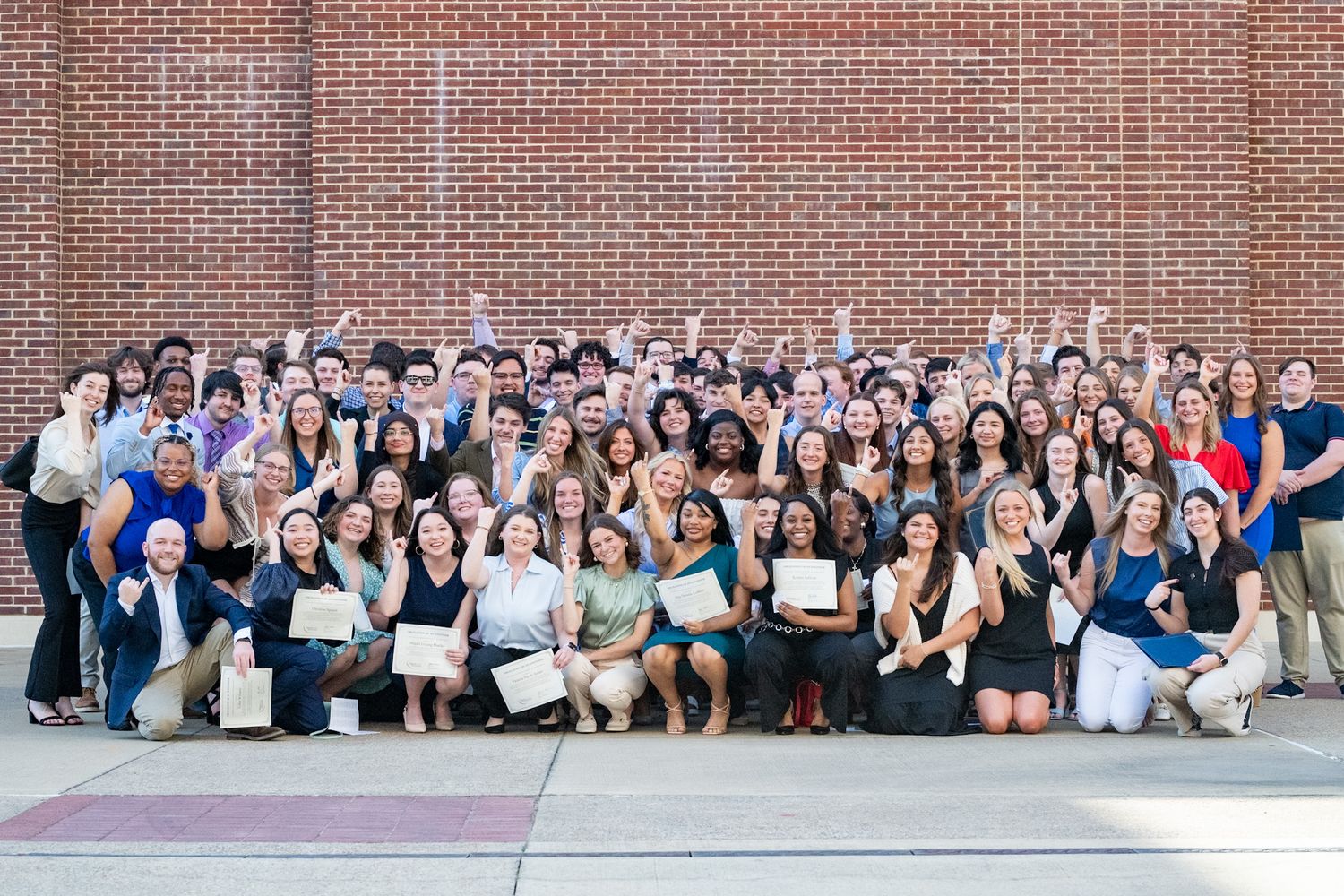 Large group of students and faculty members pose together for a photo outside a brick building.
