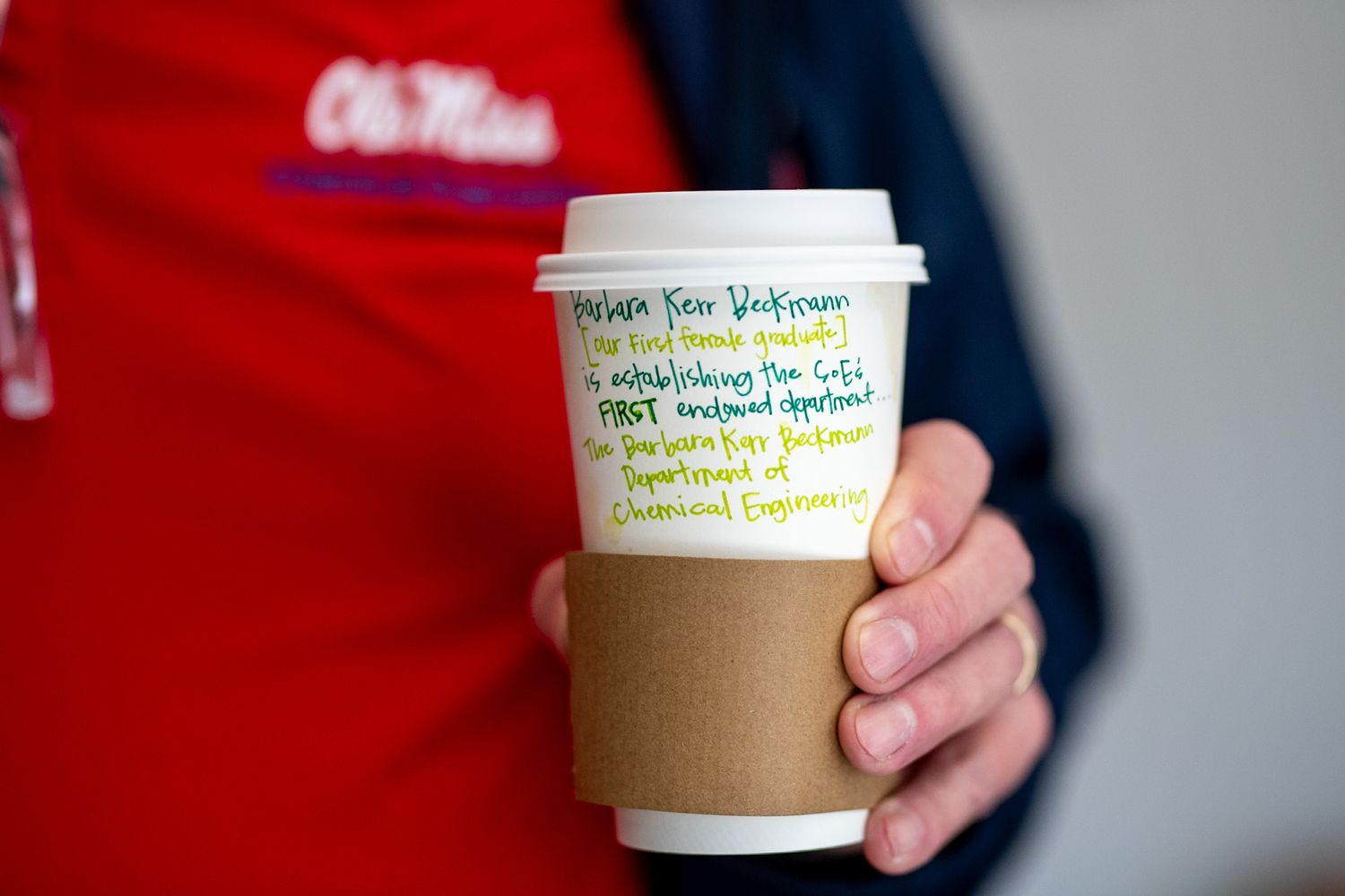Hand holding a Ole Miss branded coffee cup with handwritten notes in colorful ink on the white paper cup.