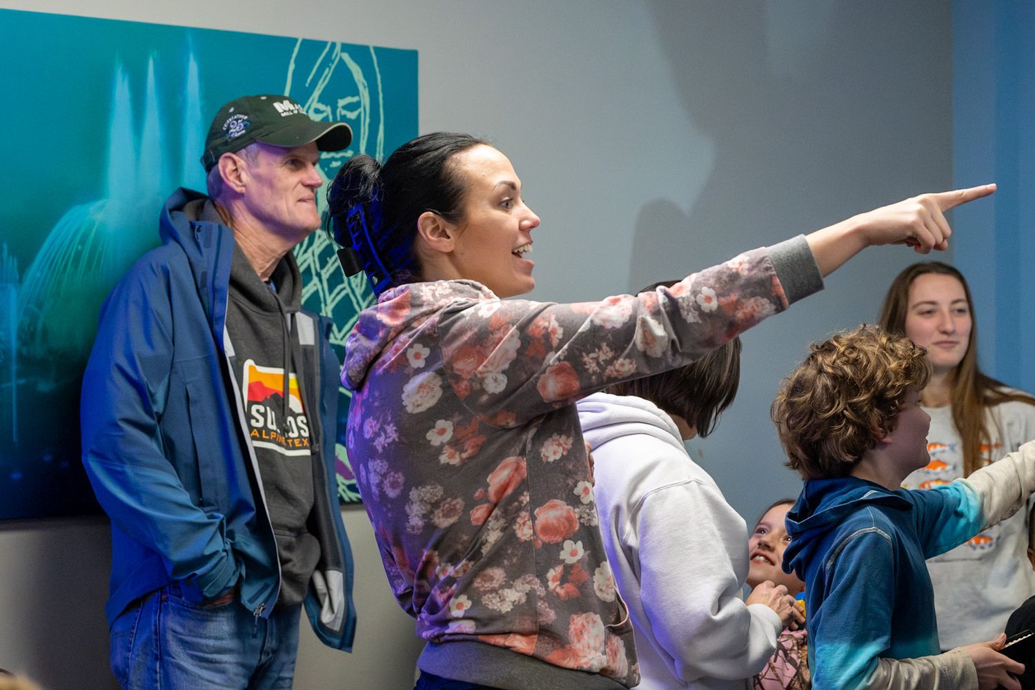 A woman enthusiastically points while speaking to a group of people in a casual indoor setting.