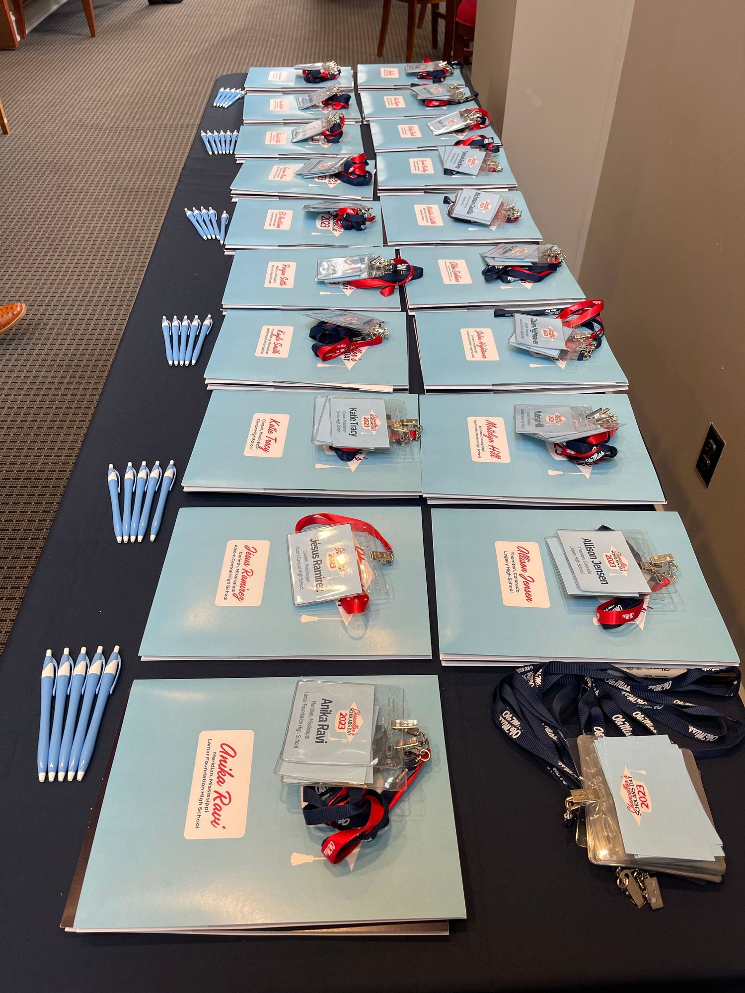 Conference registration table with blue folders, lanyards, badges, pens, and event materials neatly arranged in rows.