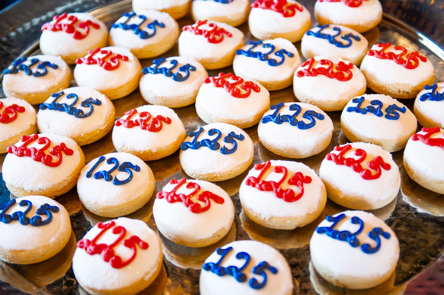 Donuts decorated with red and blue frosting displaying the number 125 on white icing, arranged on a silver tray.