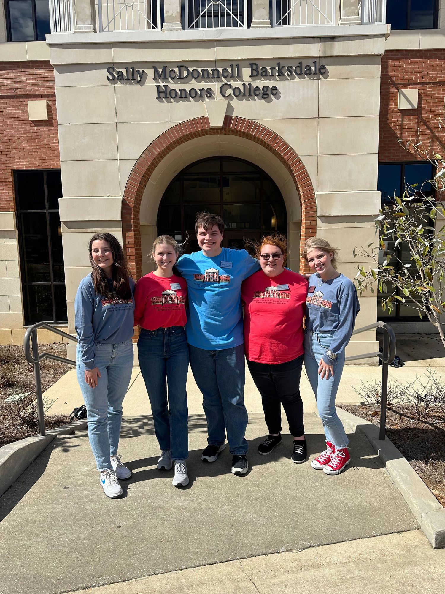 Five students pose outside Sally McDonnell Barksdale Honors College building on a sunny day.