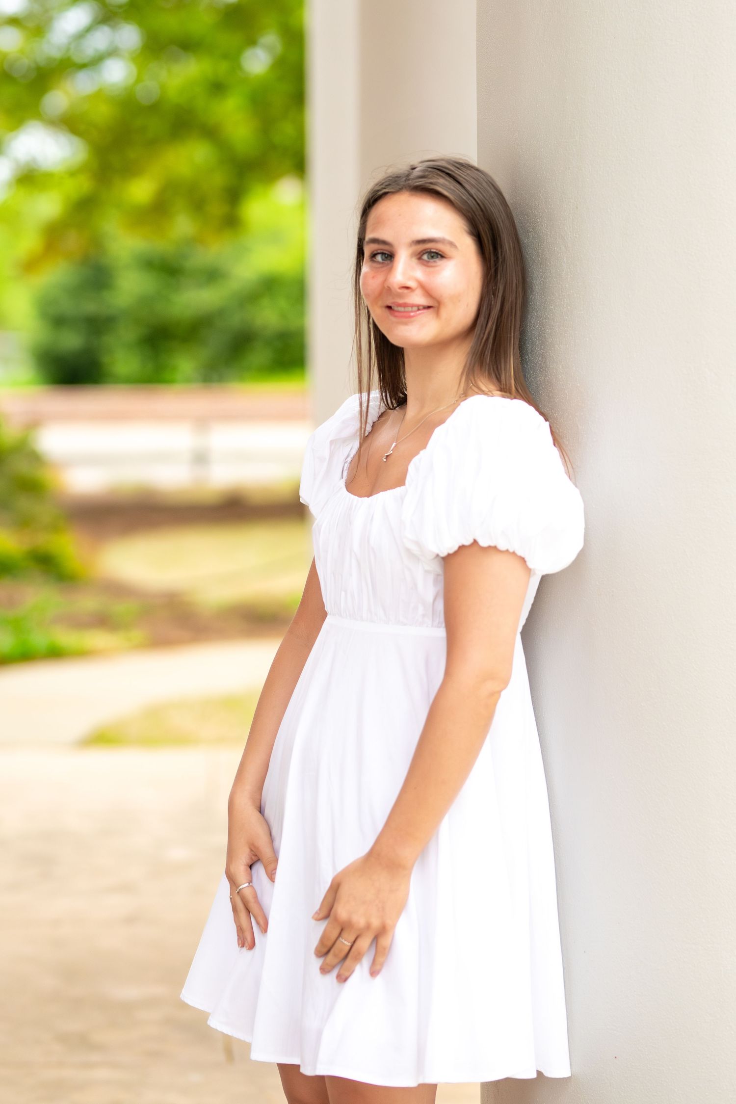 Outdoor portrait session showing someone in a flowing white summer dress against a light architectural column.