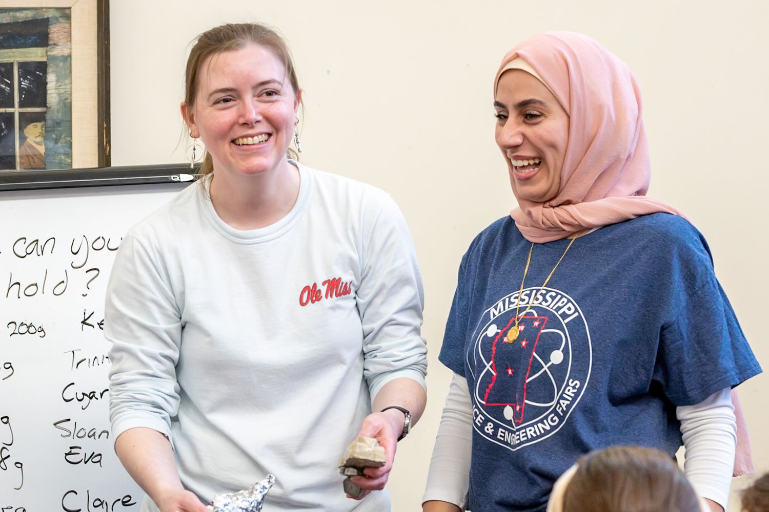 Two smiling women stand together, one wearing an Ole Miss shirt and the other a Mississippi Science & Engineering shirt.