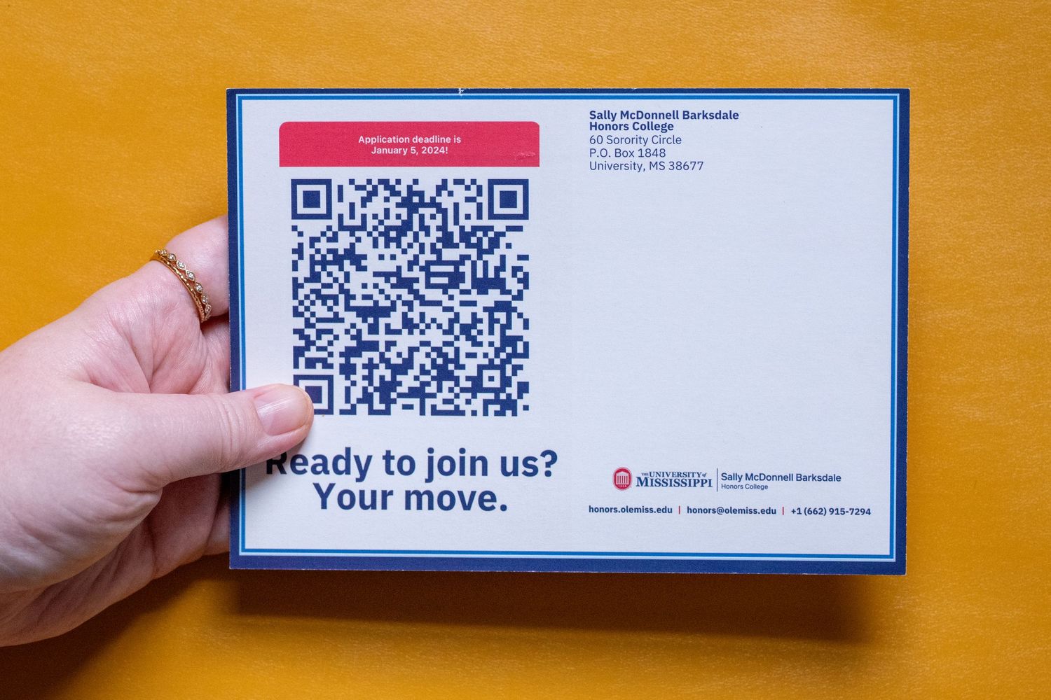 Hand holding a university mailer with QR code and 'Ready to join us? Your move.' recruitment message.