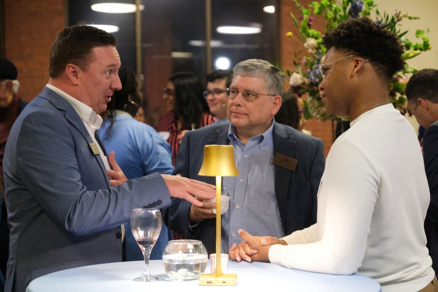 Three men in business attire engage in conversation around a high-top table at a networking event.