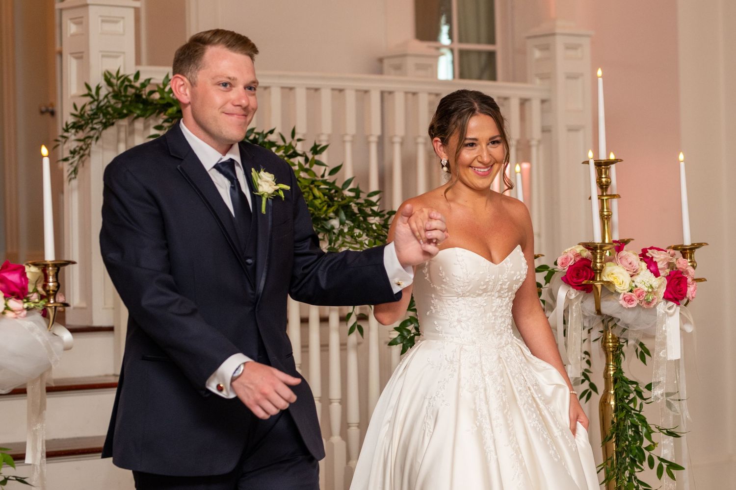 Bride and groom smiling at wedding ceremony altar with floral arch and candles.