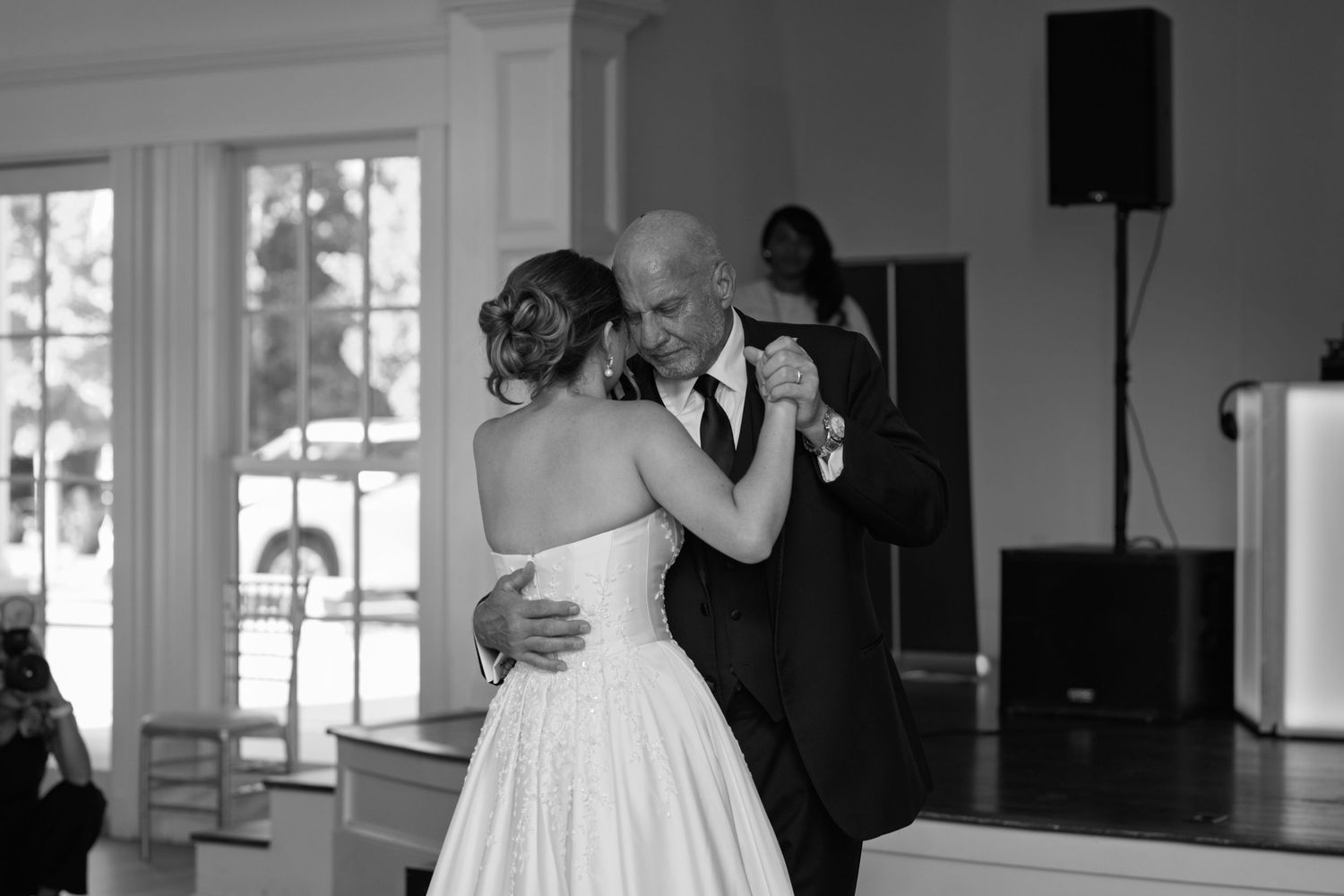 A heartfelt black and white moment of two people sharing a dance in an elegant ballroom with bright windows.