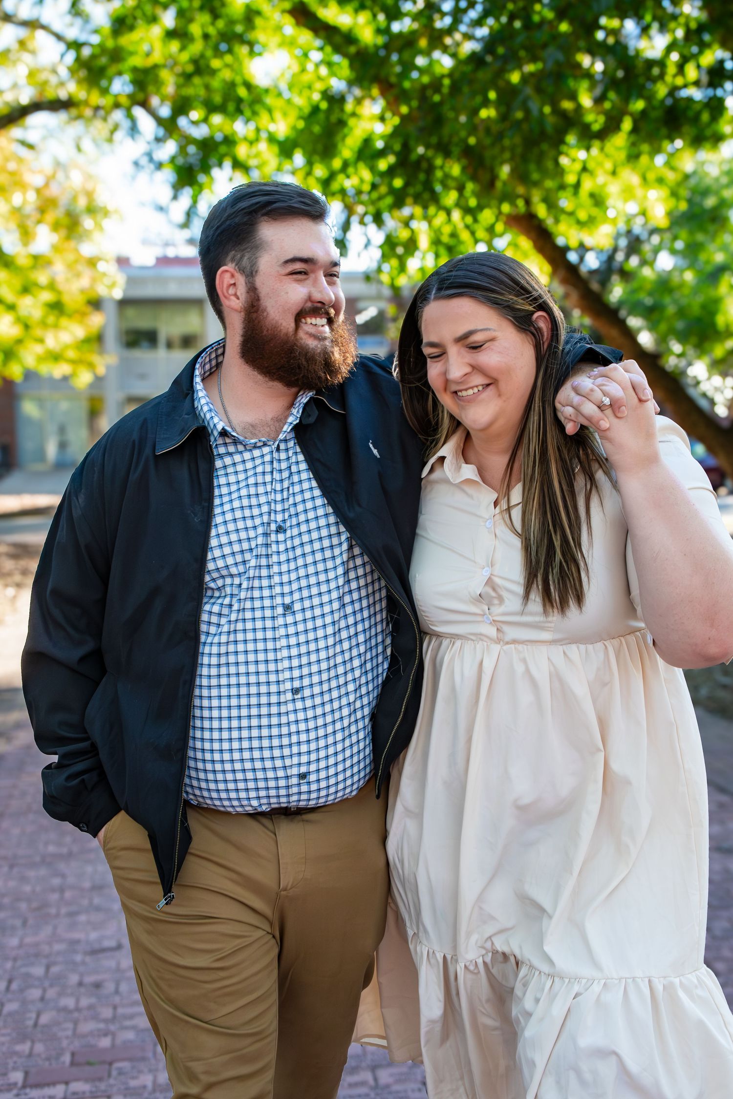 A couple enjoying a romantic walk together on a brick path surrounded by green trees on a sunny autumn day.