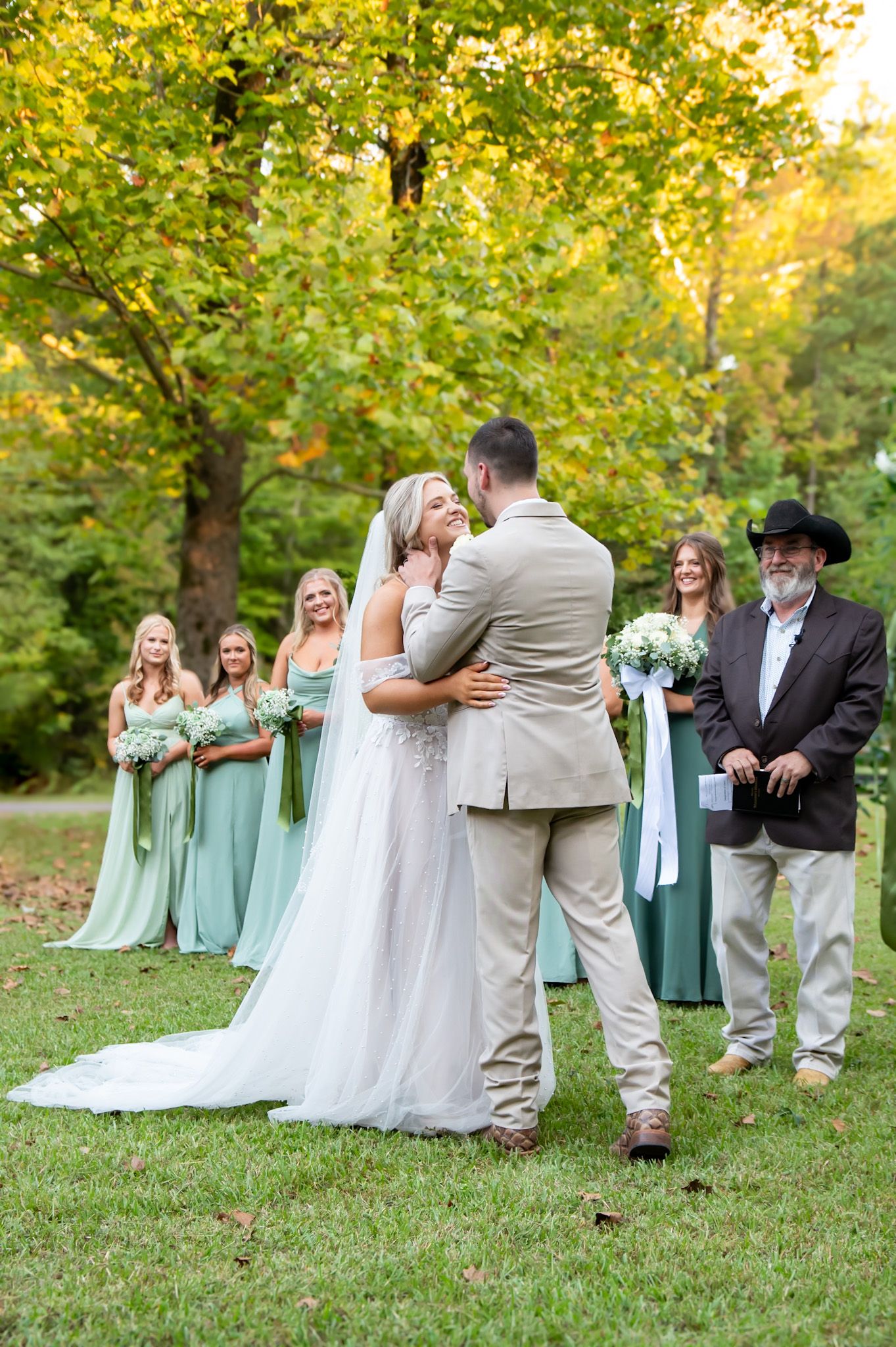 Elegant outdoor wedding ceremony in a sun-dappled forest setting with bridesmaids in soft mint green dresses.