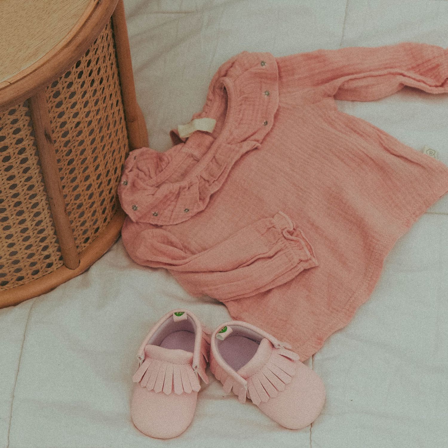 Pink baby outfit with matching moccasins arranged on light fabric. Photo shot by Mikiah Nicole Dixon