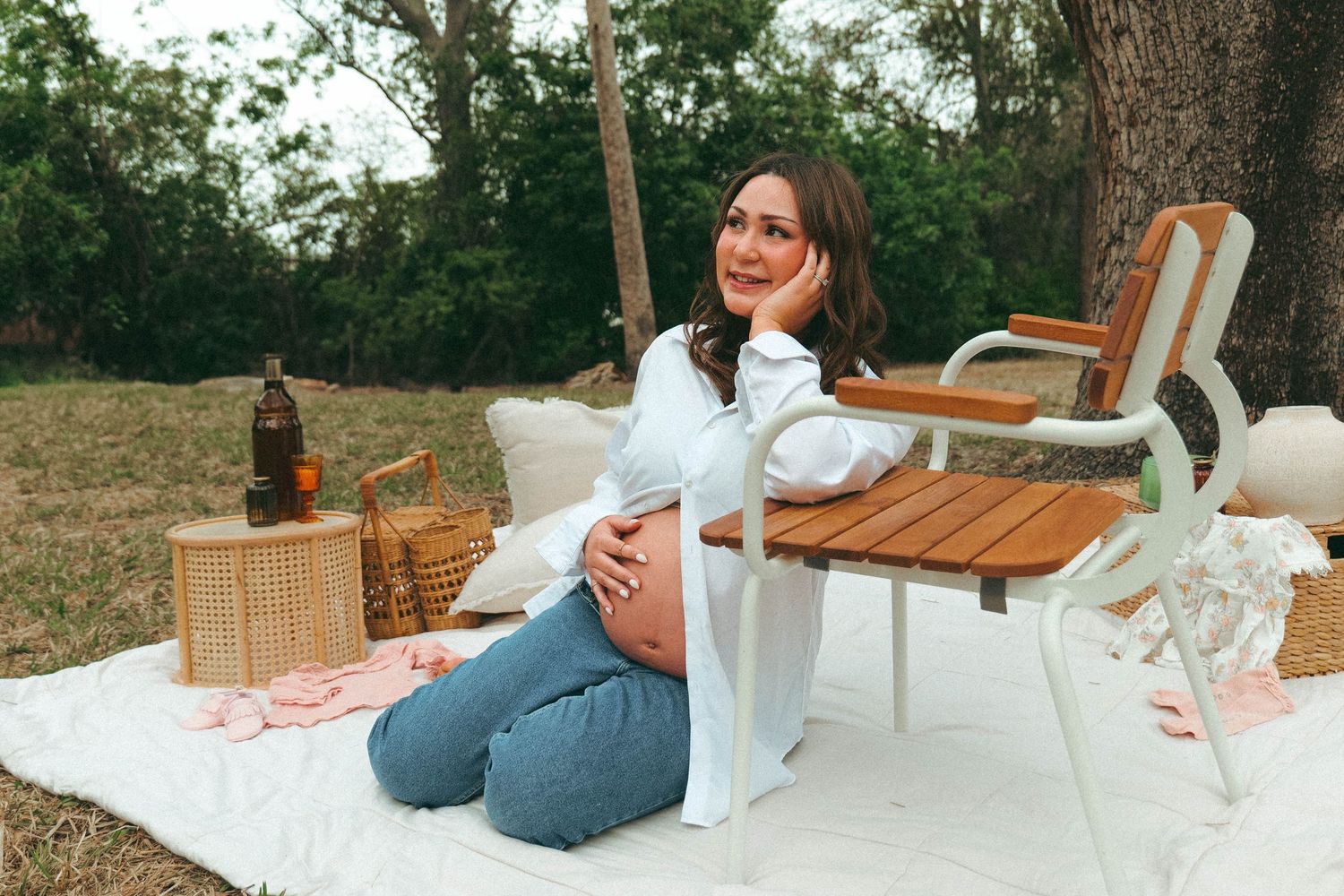 A picnic scene with a blanket, wine bottle, and wooden chair set up outdoors on a sunny day. Photo shot by Mikiah Nicole Dixon