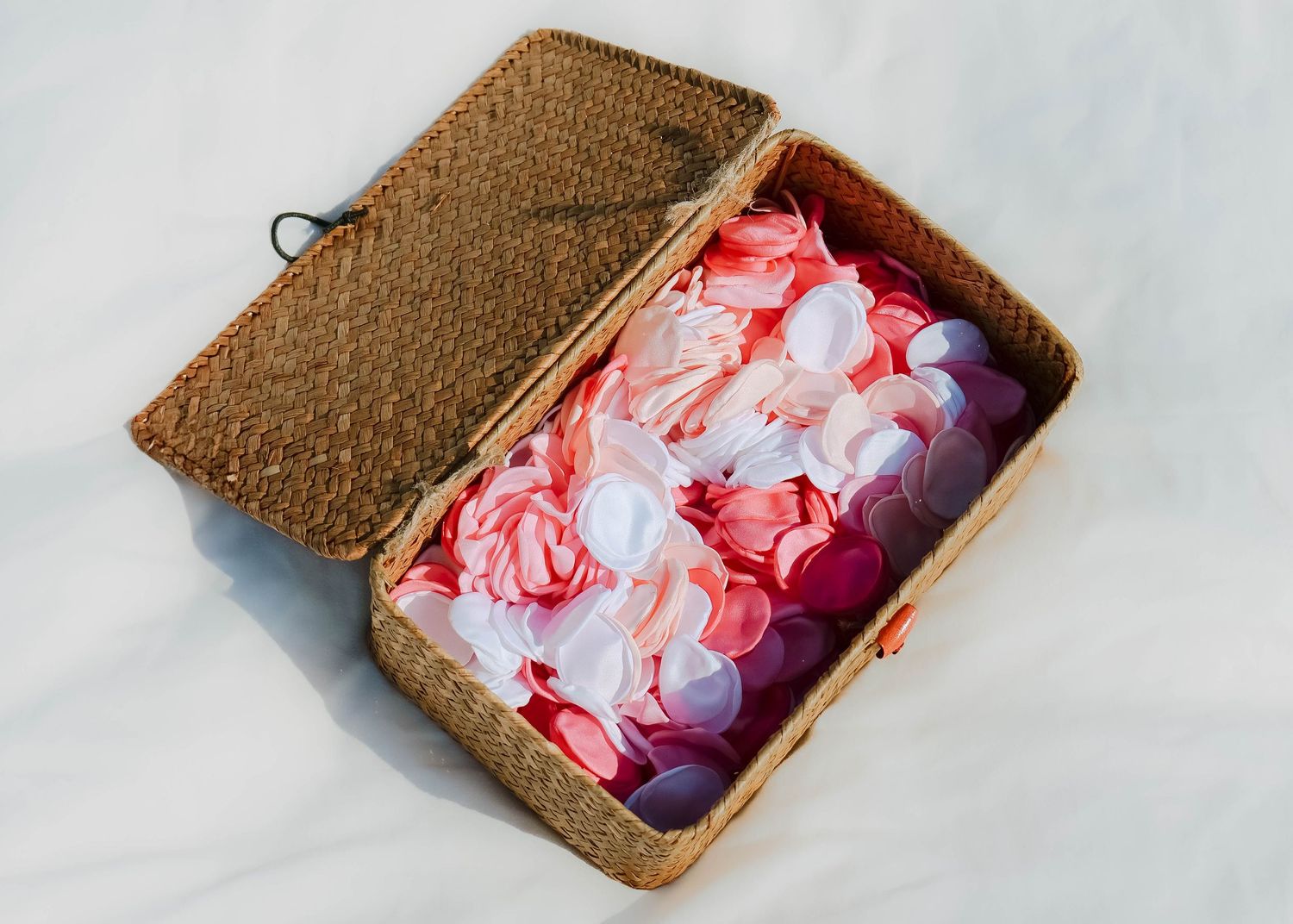 Wicker basket filled with pink and white floral petals on white background. Photo shot by Mikiah Nicole Dixon