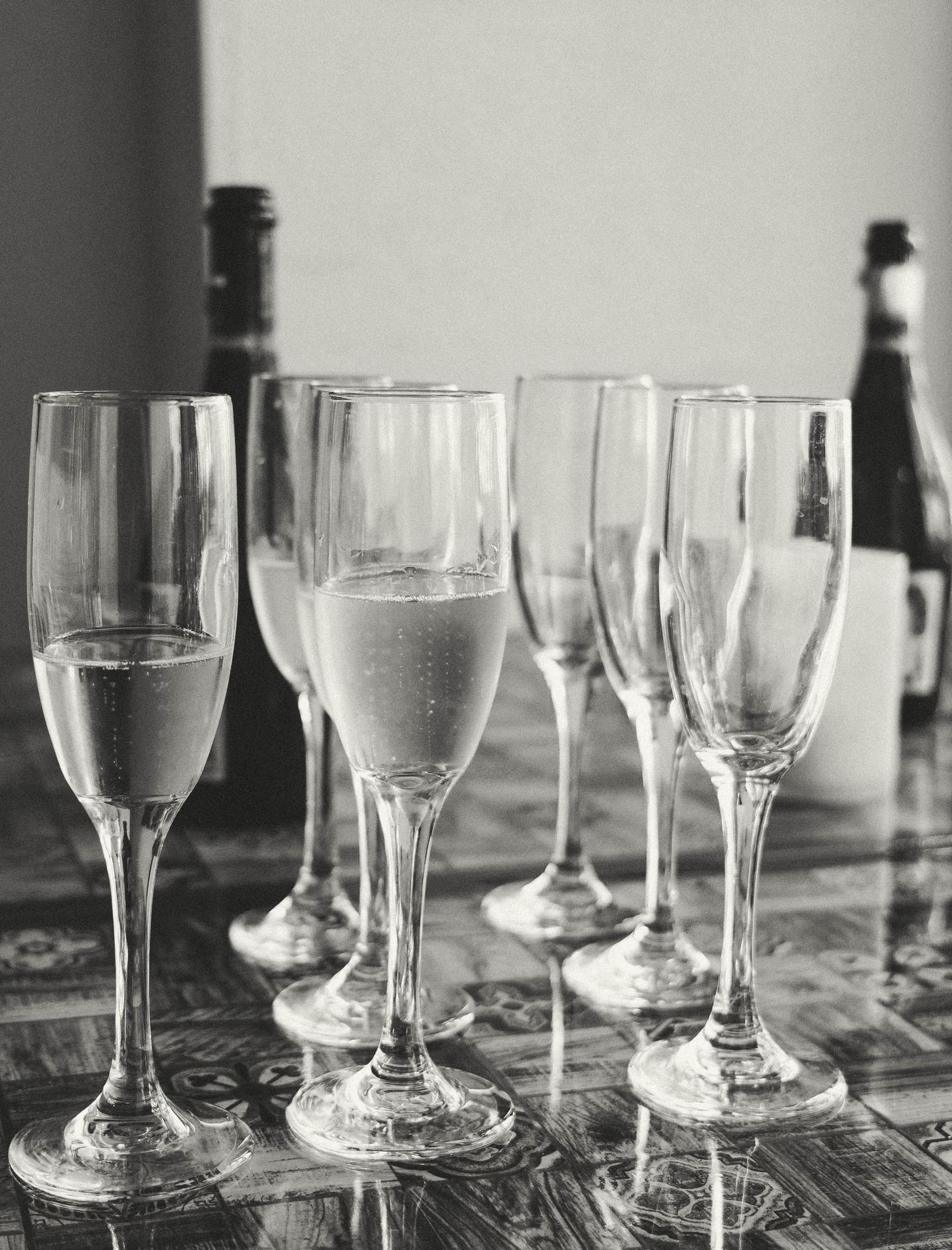 Elegant champagne flutes and wine glasses arranged on a reflective surface in black and white. Photo shot by Mikiah Nicole Dixon
