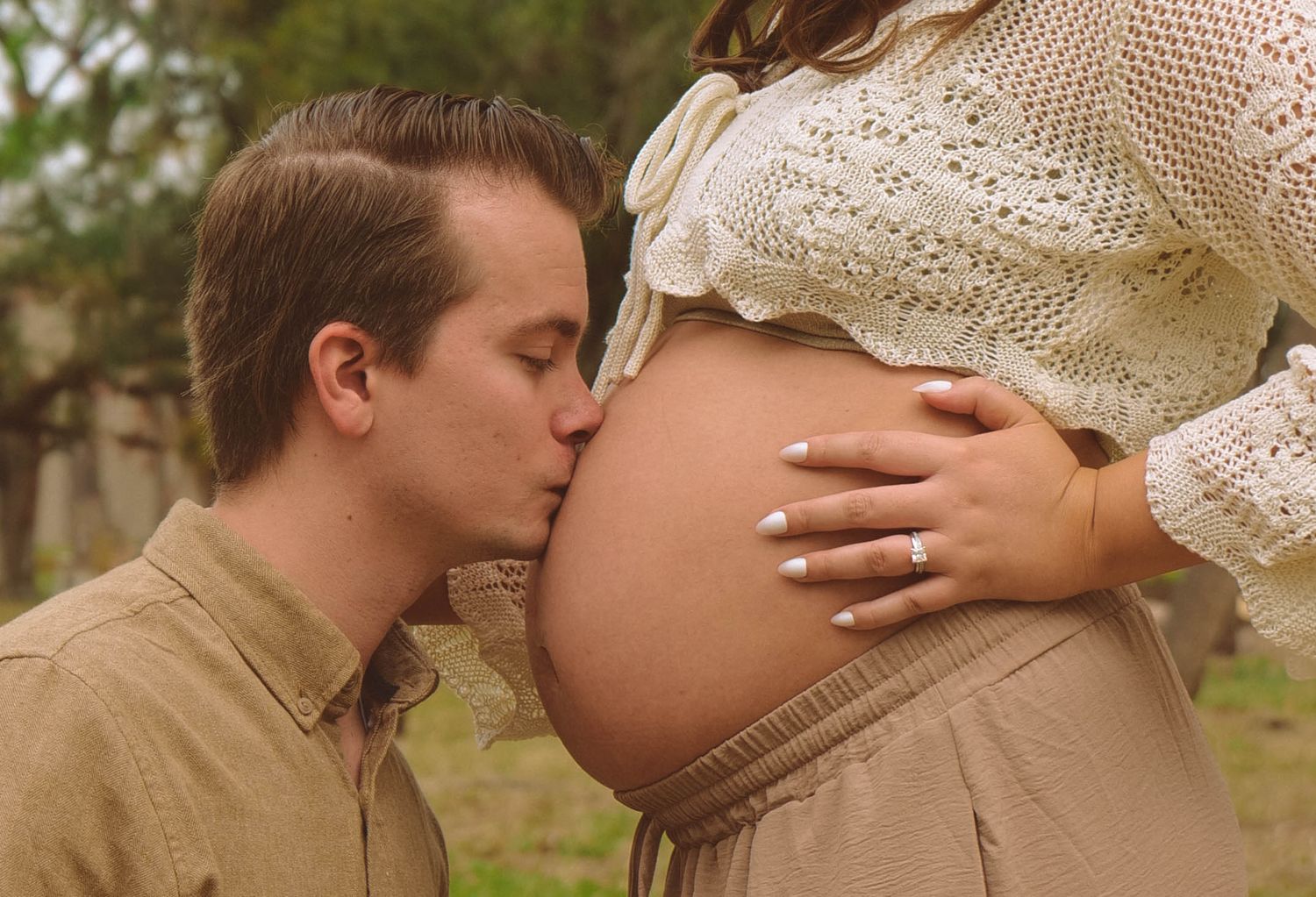 A tender maternity moment captured outdoors with a pregnant belly in a cream lace top. Photo shot by Mikiah Nicole Dixon