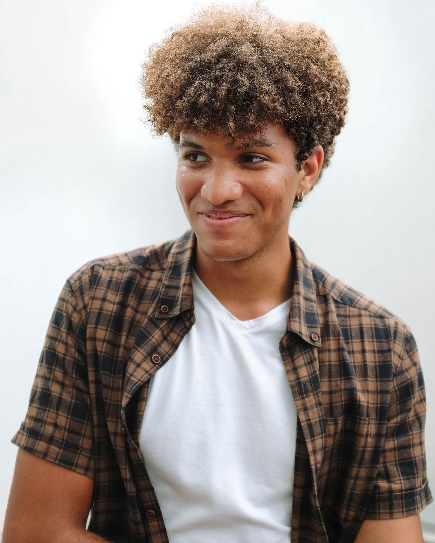 Casual portrait with warm smile wearing plaid shirt and white t-shirt. Photo shot by Mikiah Nicole Dixon