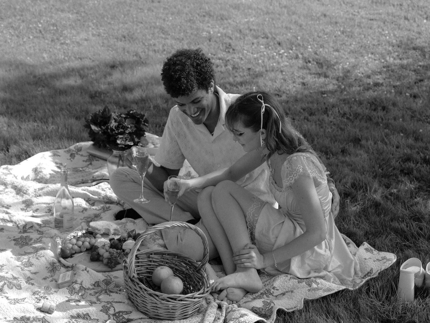 Black and white photo of people enjoying a casual outdoor picnic on a blanket. Photo shot by Mikiah Nicole Dixon