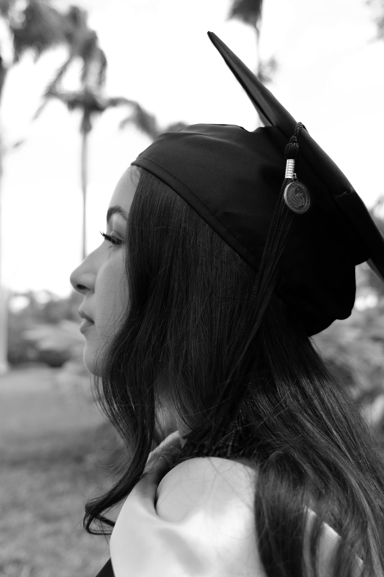 Black and white profile shot of graduate wearing cap against palm tree background. Photo shot by Mikiah Nicole Dixon