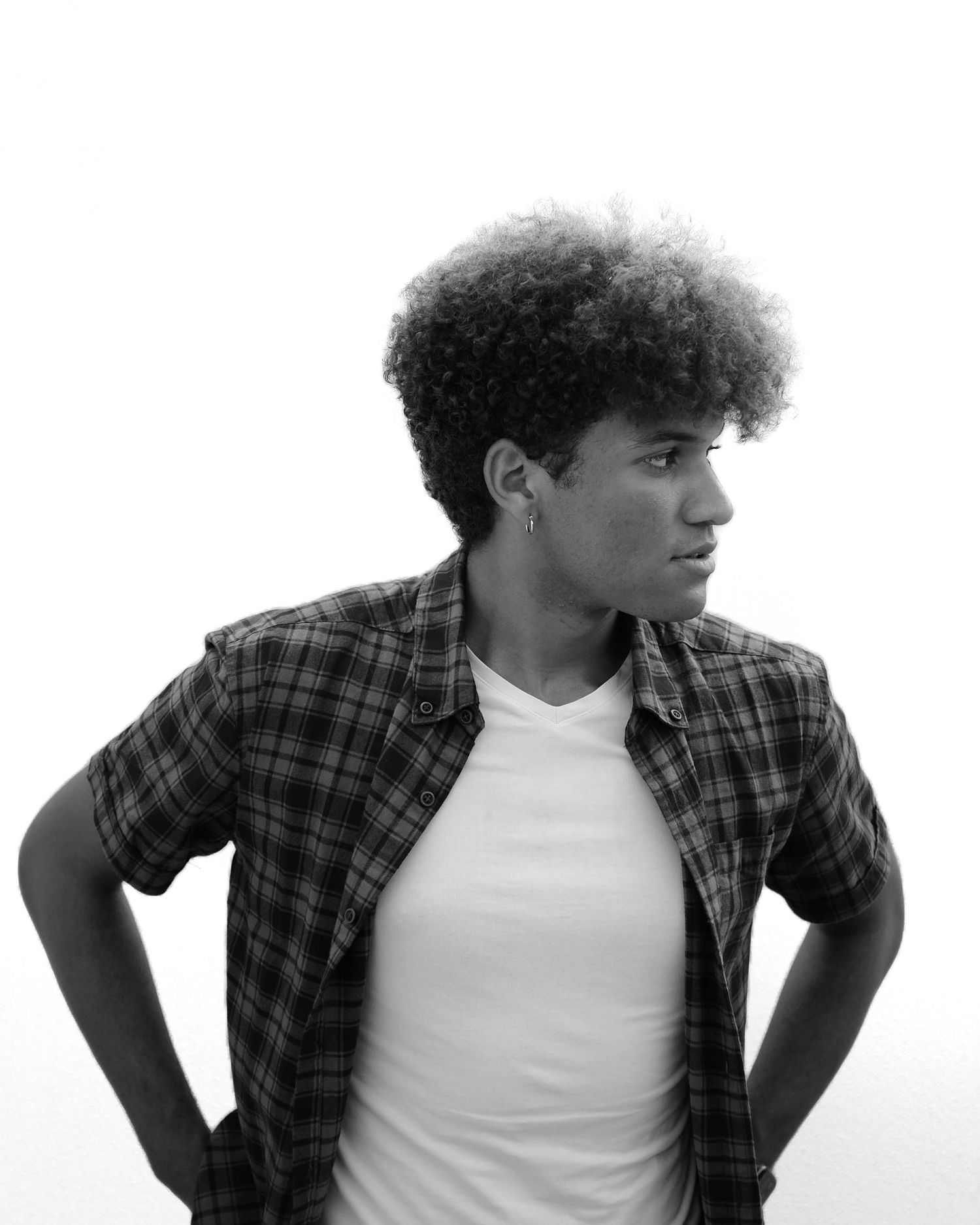 Portrait of person in plaid shirt and white tee with curly hair looking to the side. Photo shot by Mikiah Nicole Dixon