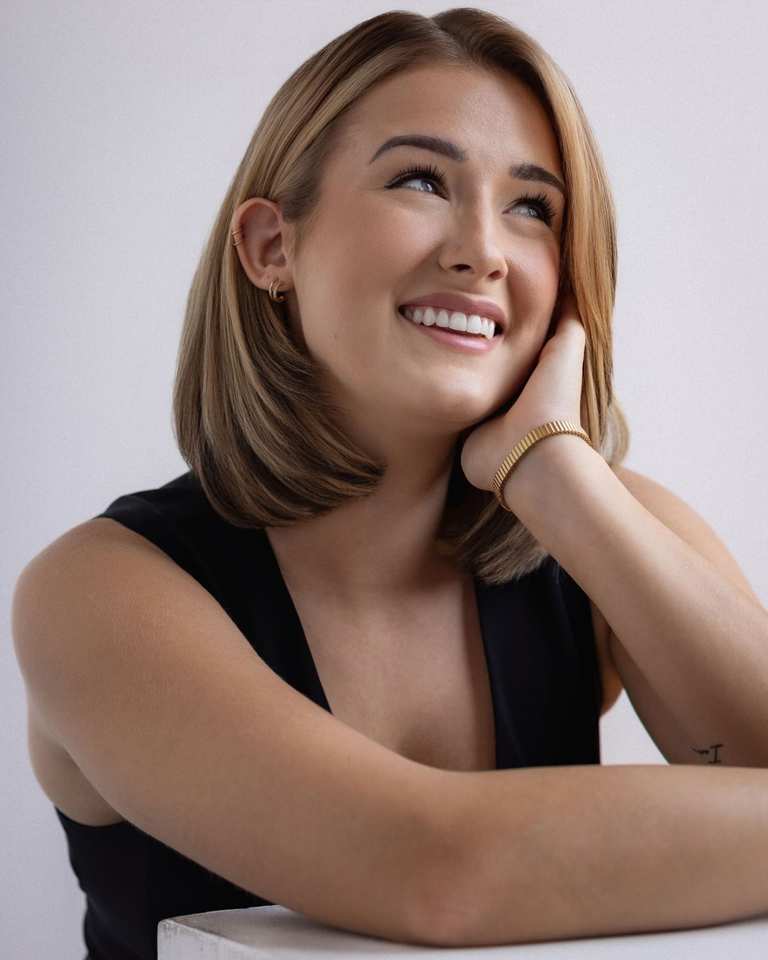 A person in a black top named Mikiah Nicole Dixon leans forward and poses expressively against a light background with natural lighting.