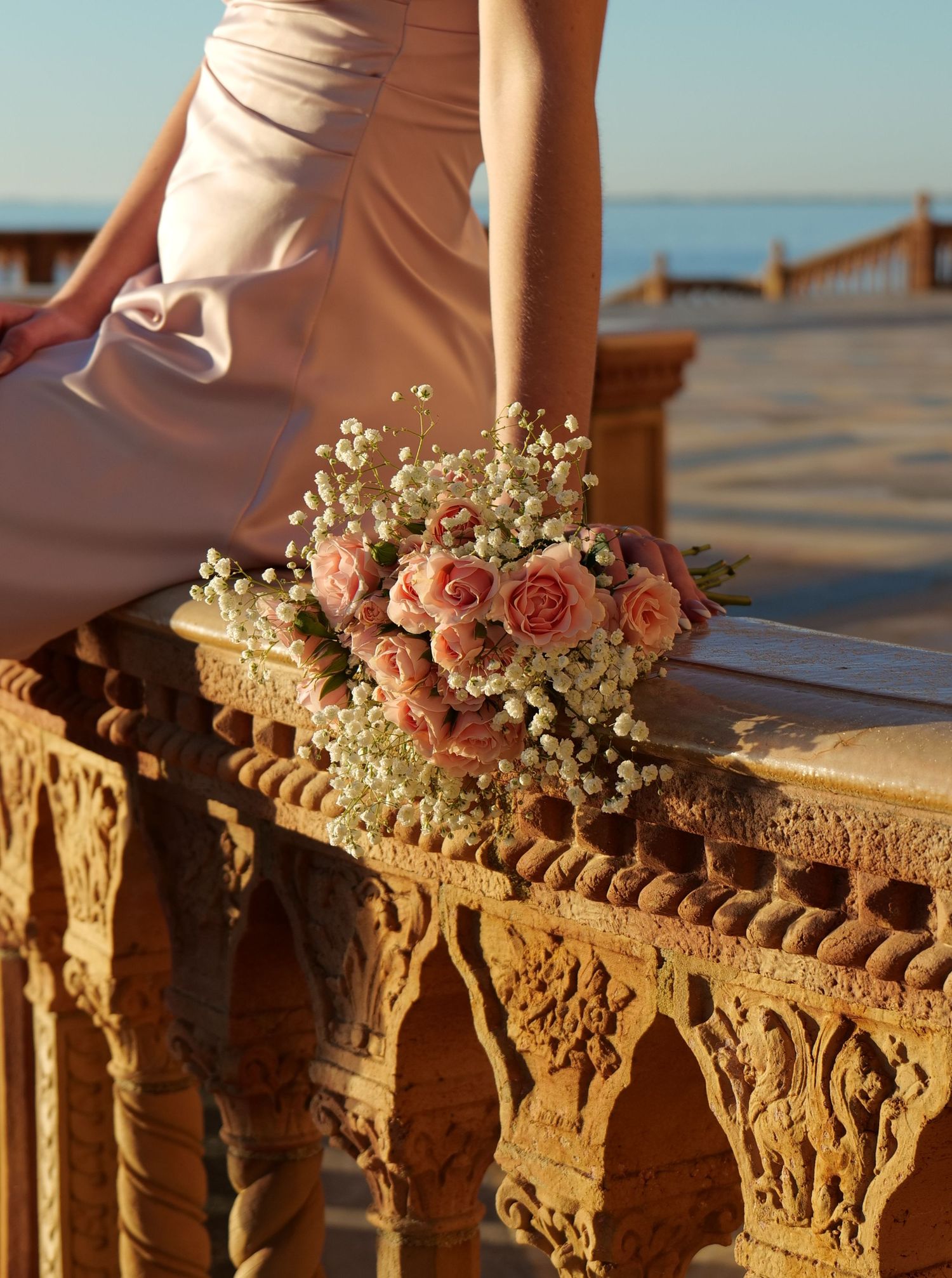 Pink and white floral bouquet rests on ornate stone railing during sunset. Photo shot by Mikiah Nicole Dixon