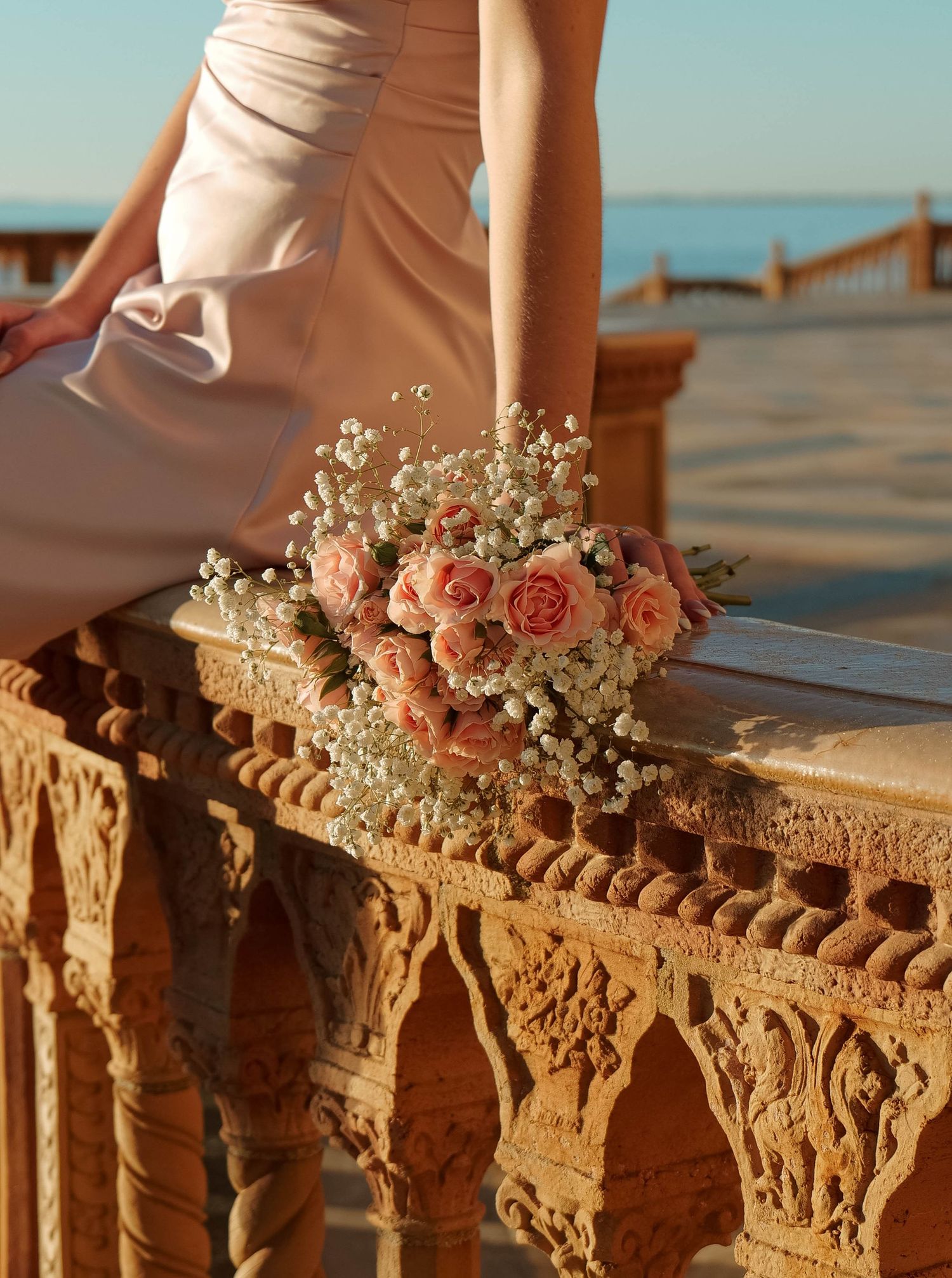 Pink roses and baby's breath bouquet rests on ornate stone railing at sunset. Photo shot by Mikiah Nicole Dixon