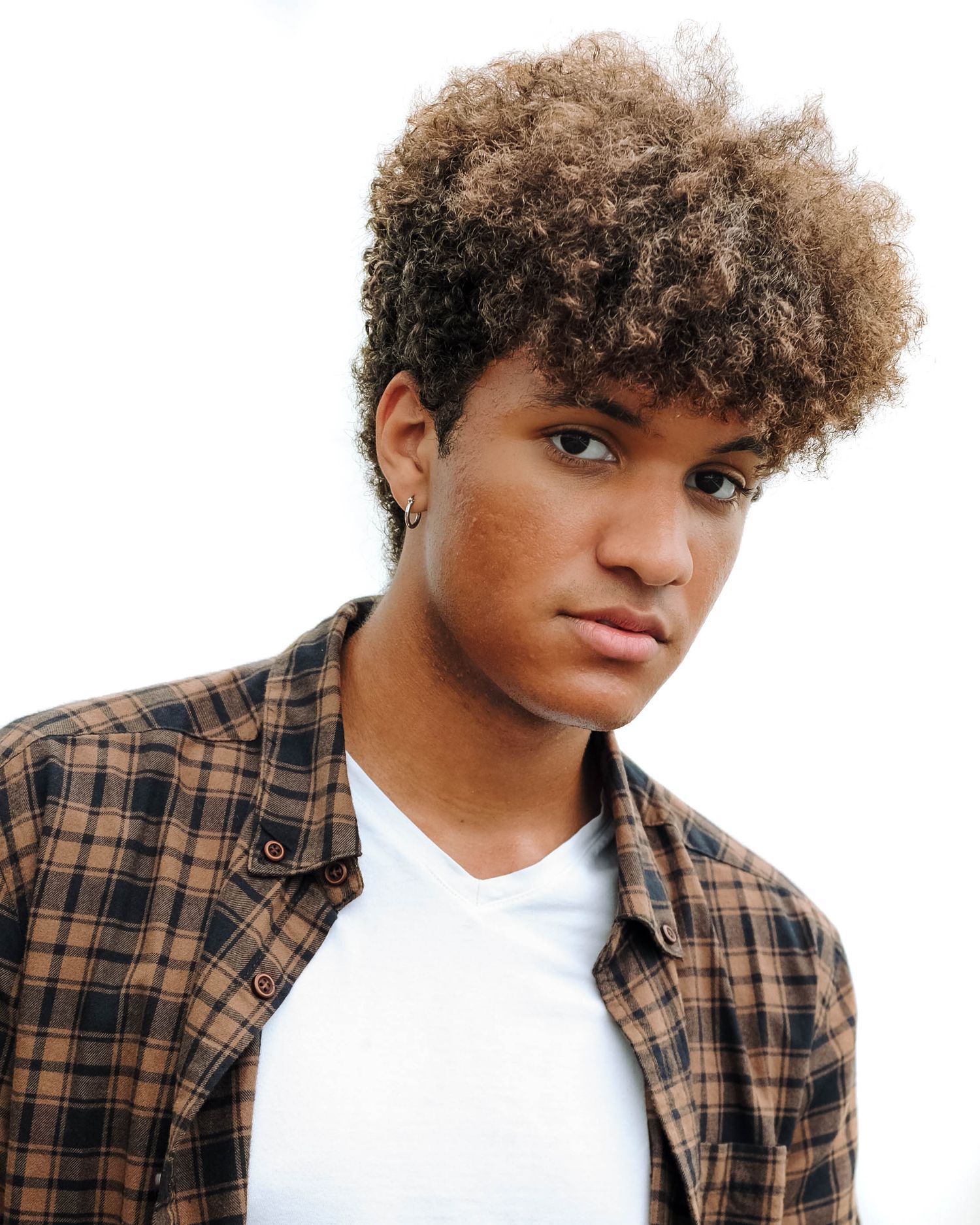 Stylish portrait featuring curly hair, plaid shirt and white t-shirt against white background. Photo shot by Mikiah Nicole Dixon