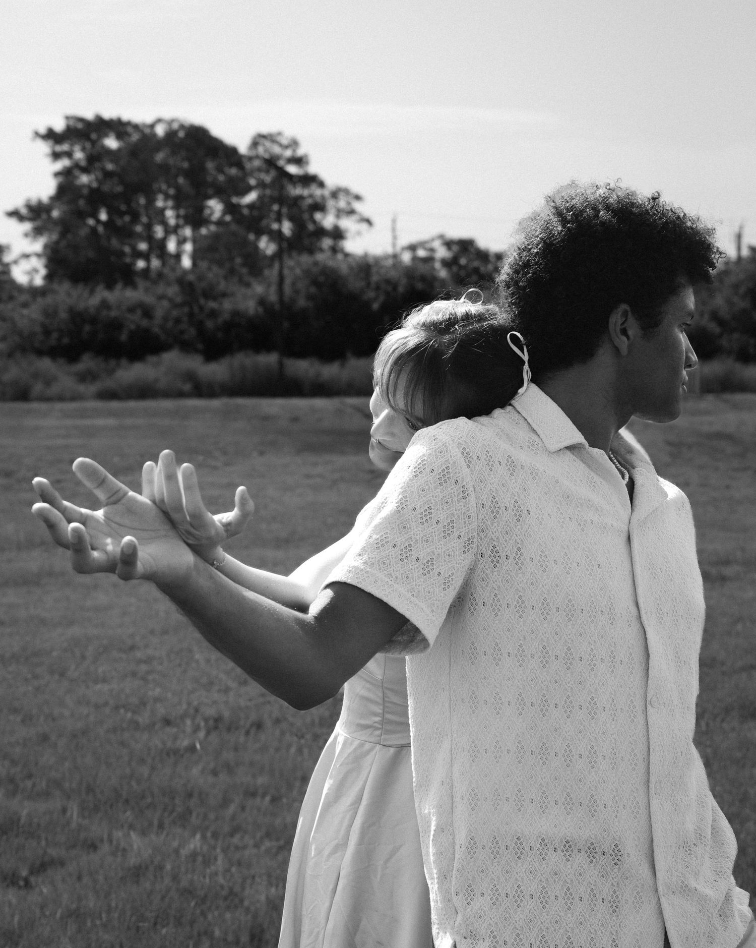 People in white outfits posing with outstretched arms in a field on a sunny day. Photo shot by Mikiah Nicole Dixon