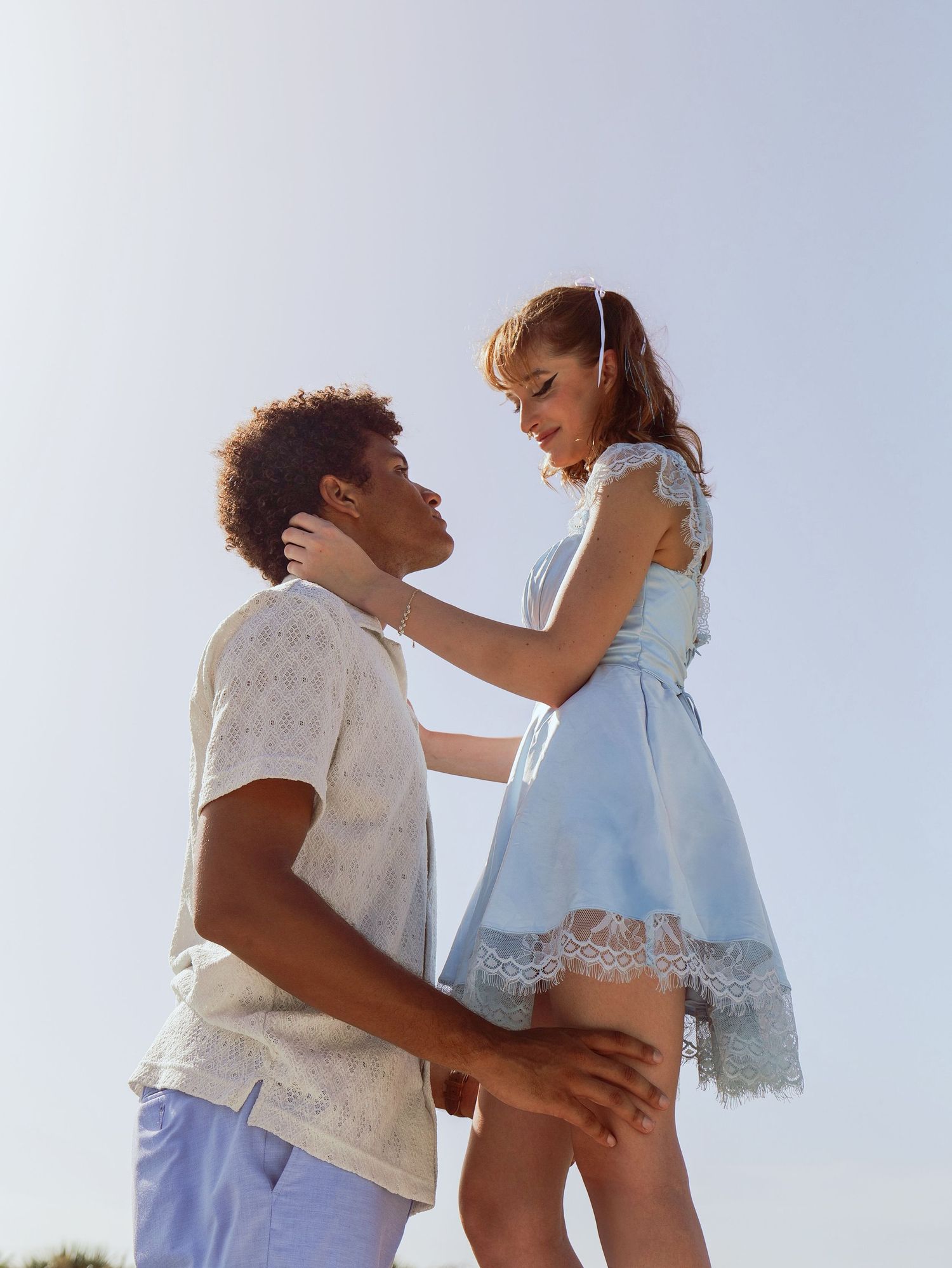 A tender romantic moment between two people in white clothing against a bright sky background. Photo shot by Mikiah Nicole Dixon
