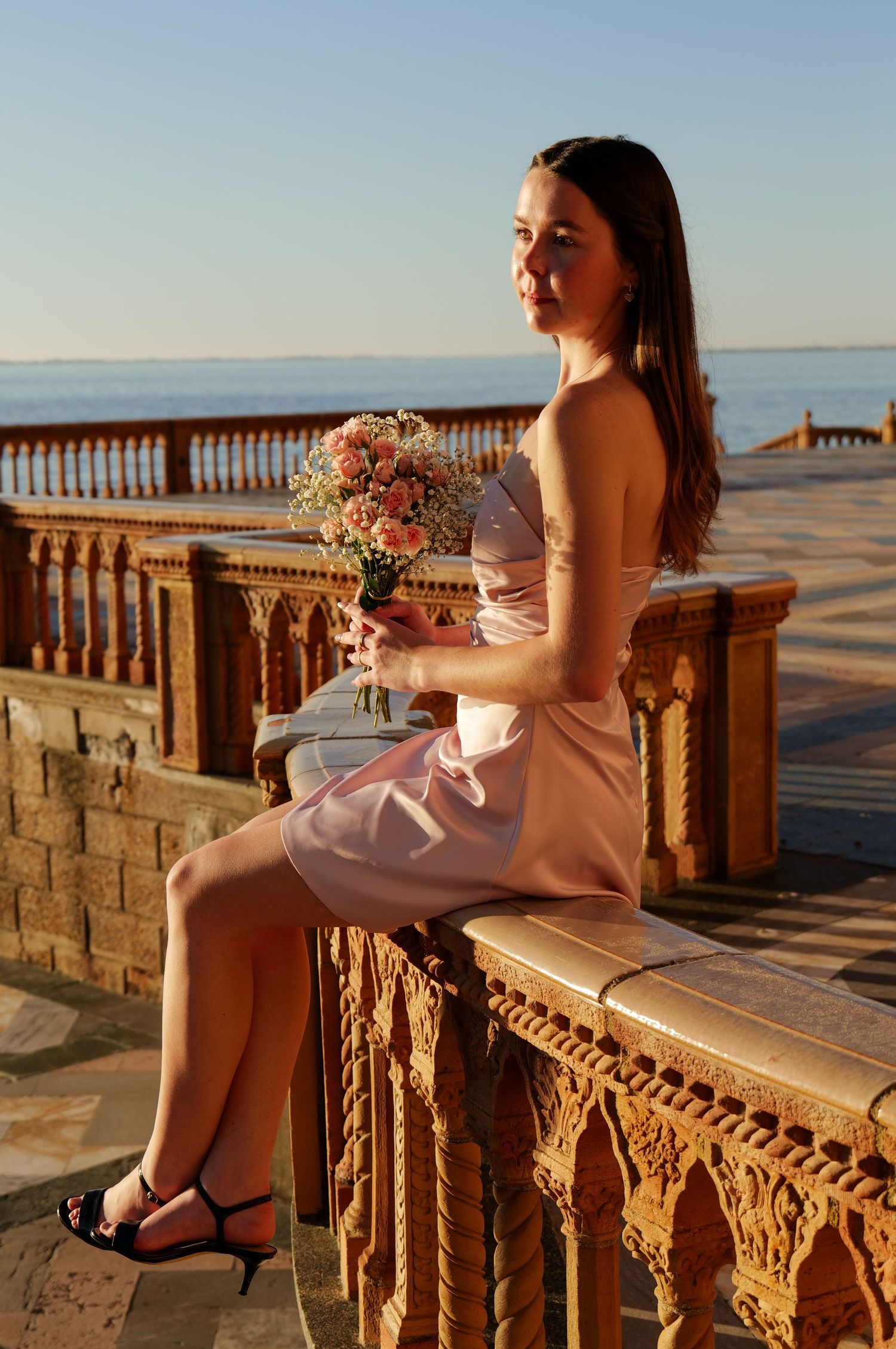 Model in strapless pink dress poses with bouquet on architectural balcony at dusk. Photo shot by Mikiah Nicole Dixon