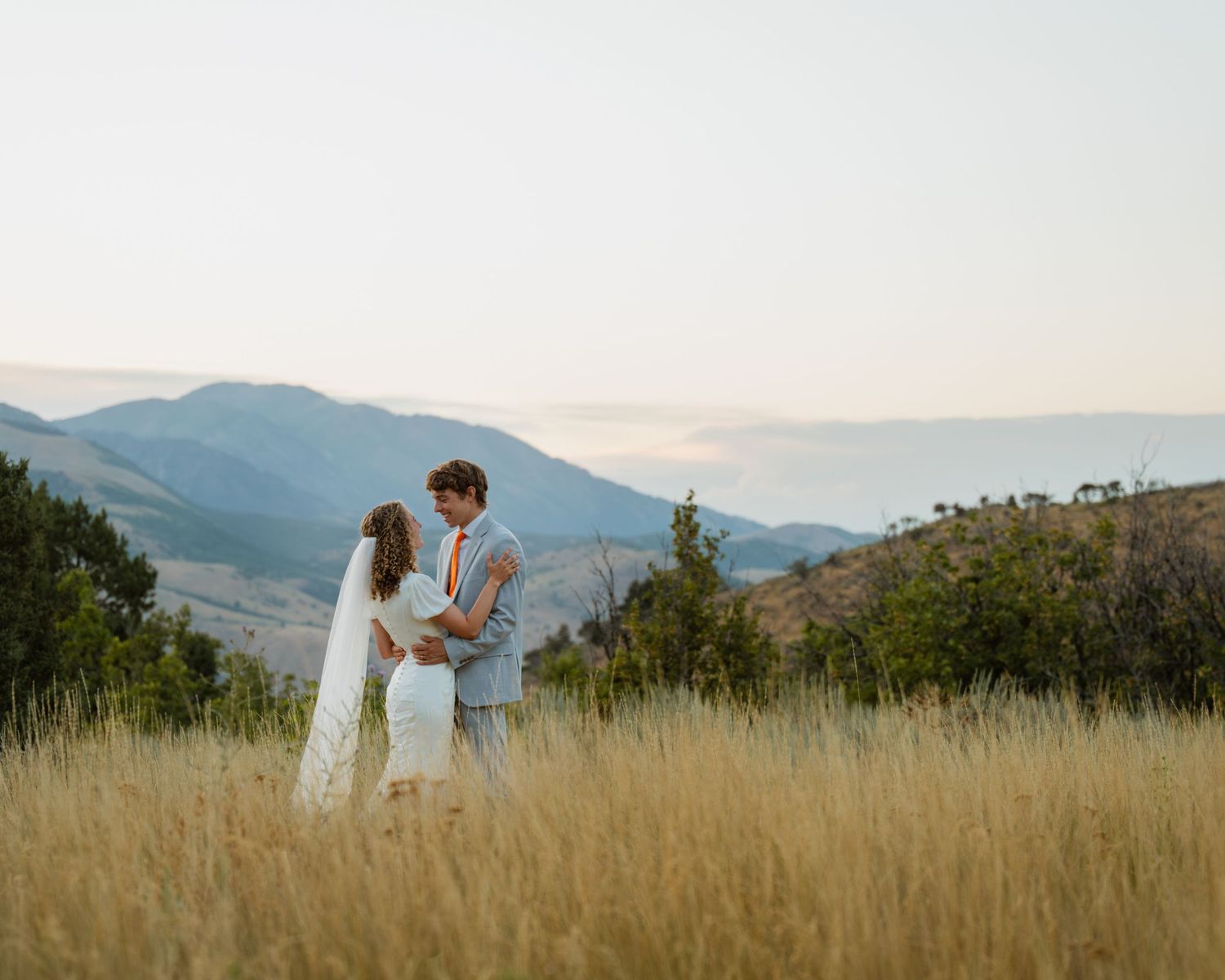 Authentic Des Moines wedding photography – bride and groom in tall grass with mountain sunset backdrop, golden hour bridal portraits.