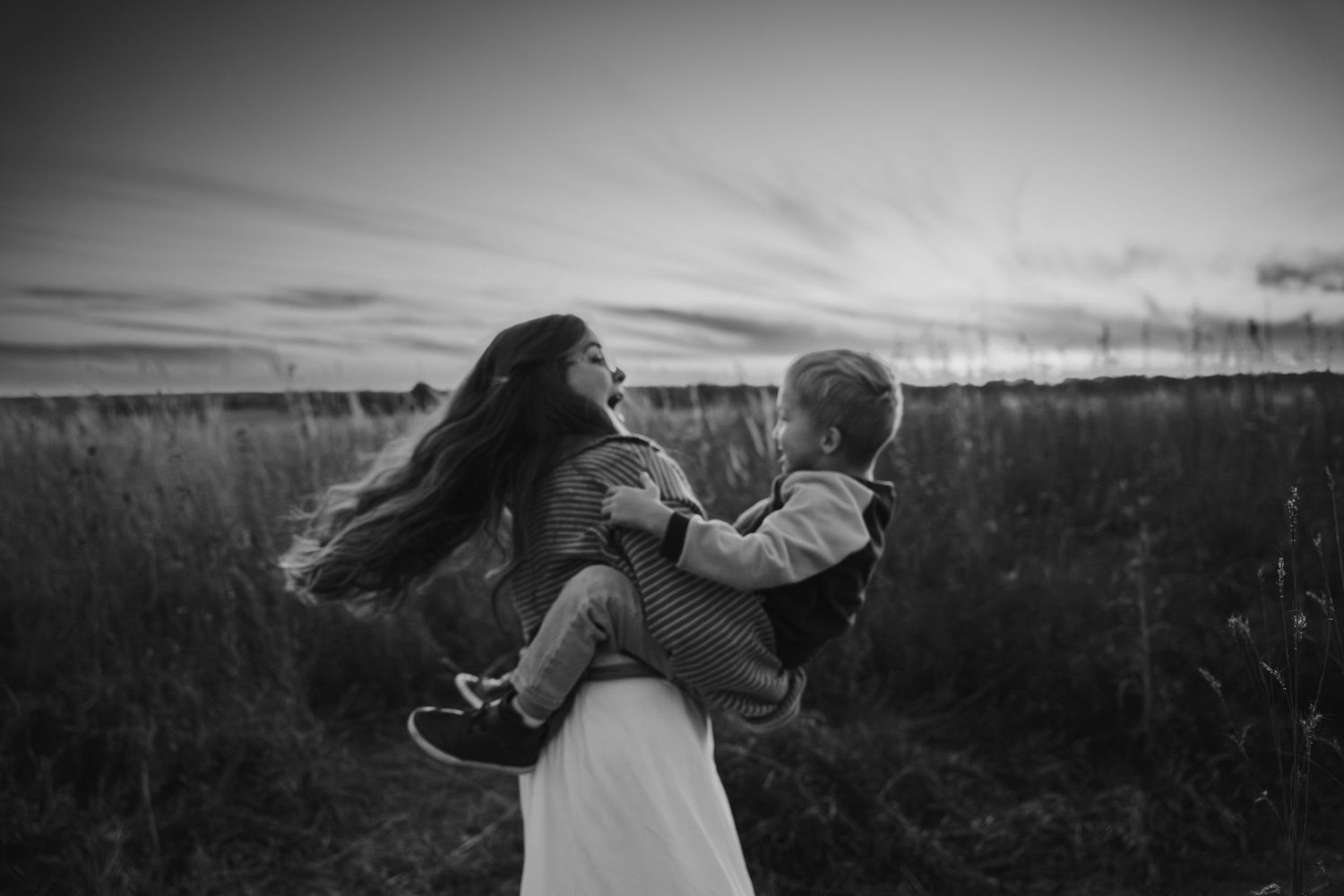 Mom spinning in circles, dancing, with her son on a beautiful evening in front of a sunset at Saylorville Lake in Des Moines, IA.
