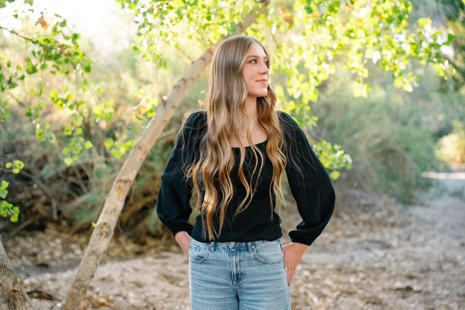 Des Moines Iowa senior portrait photographer – confident young woman with long blonde hair standing in natural greenery, soft golden light.