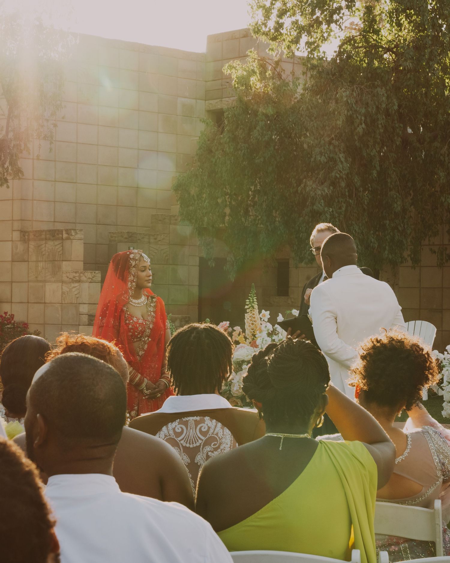 Des Moines Indian Wedding ceremony. Bride in a stunning red gown and groom in a classy white suit with a sun flare.