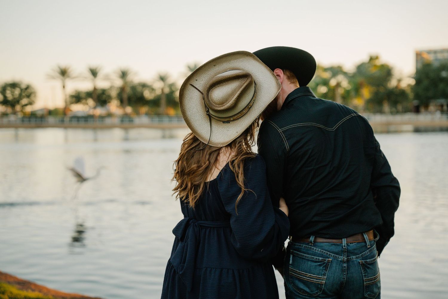 Des Moines Iowa lake engagement photographer – cowboy-western couple embracing near water, romantic and relaxed lakeside portrait.