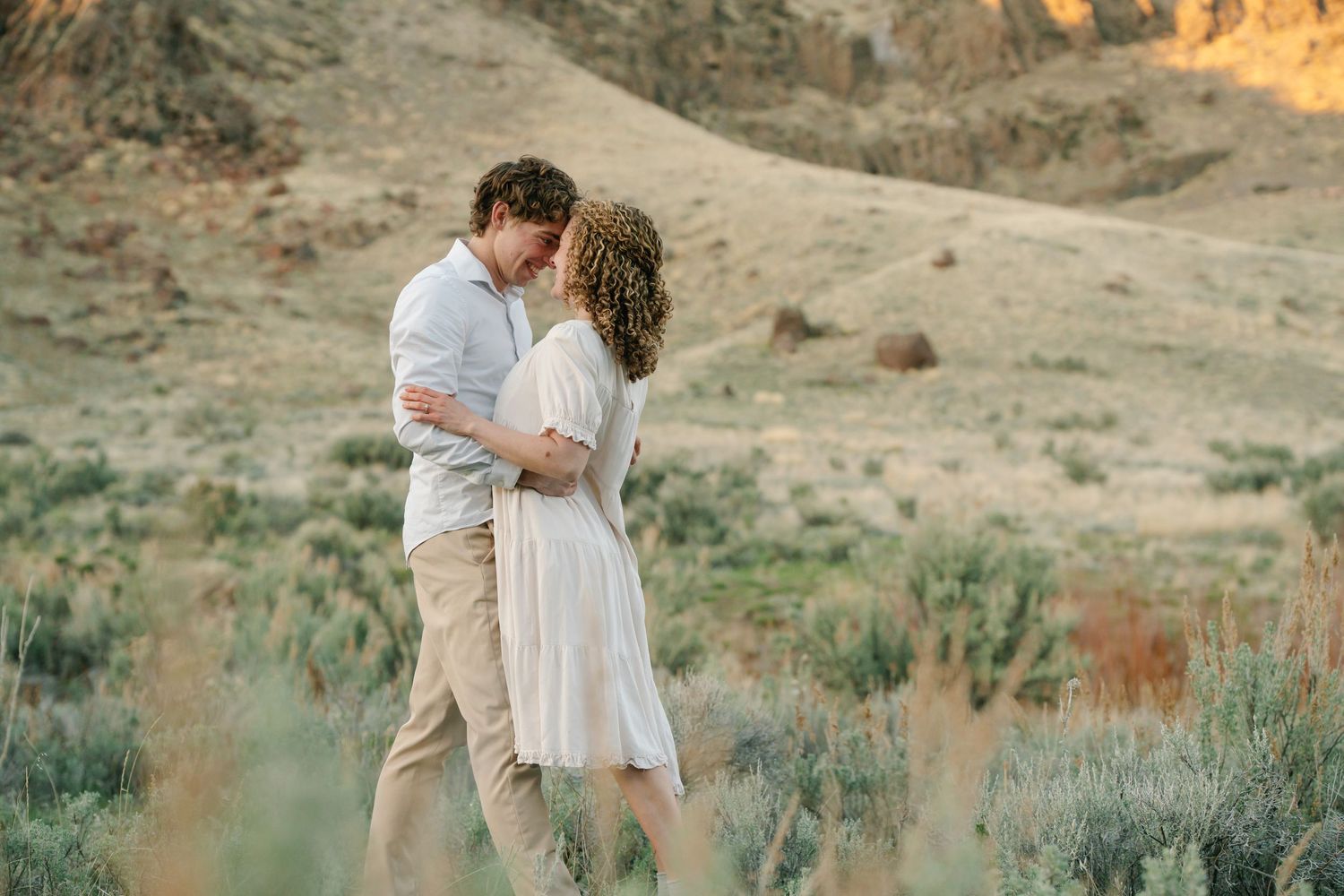Authentic Des Moines engagement photographer – formal couple portrait embracing on grassy hills at golden hour sunset