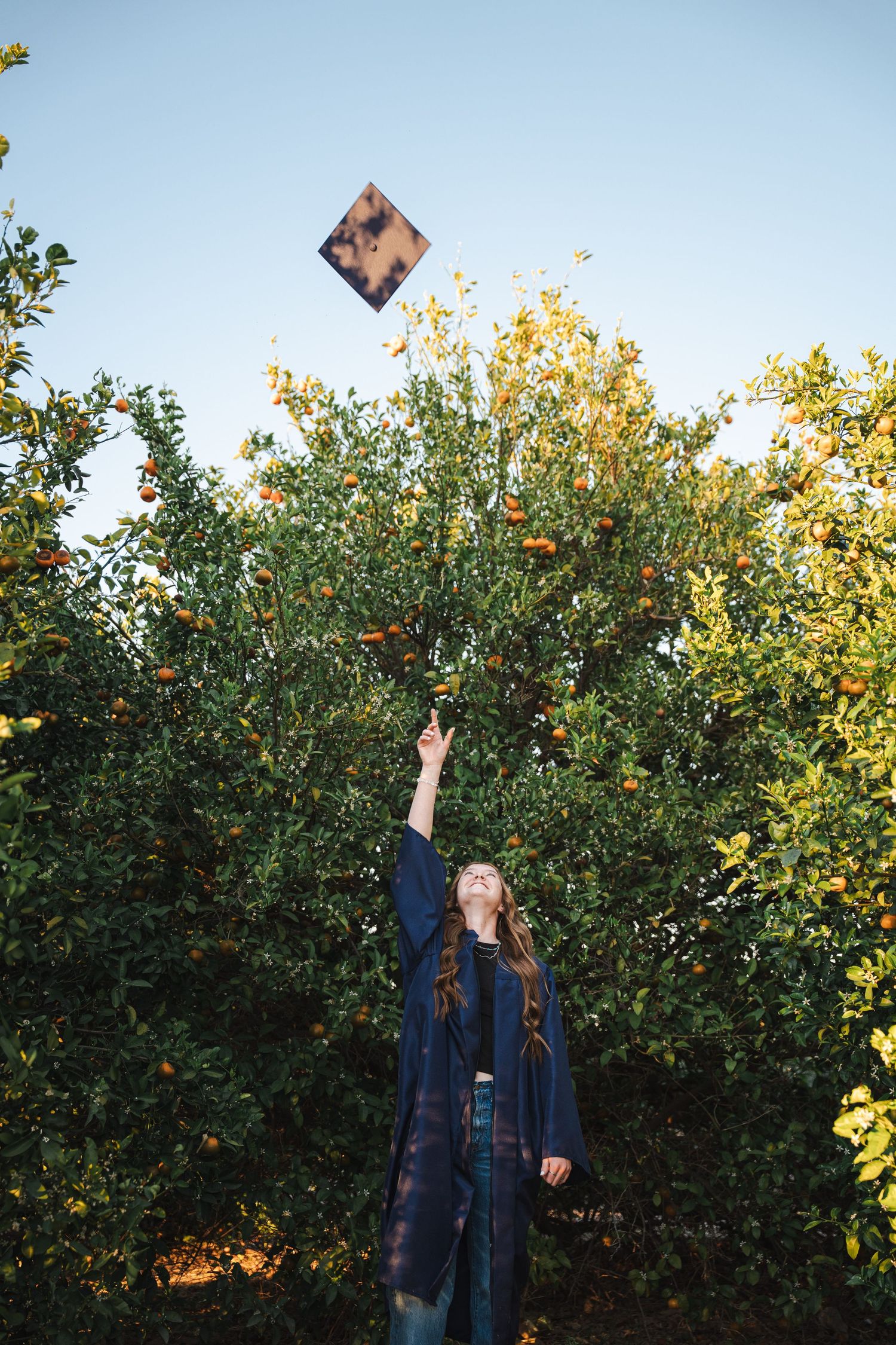 Des Moines Iowa senior portrait photographer – happy teenage girl in graduation gown with a warm smile and throwing her cap up in the air.