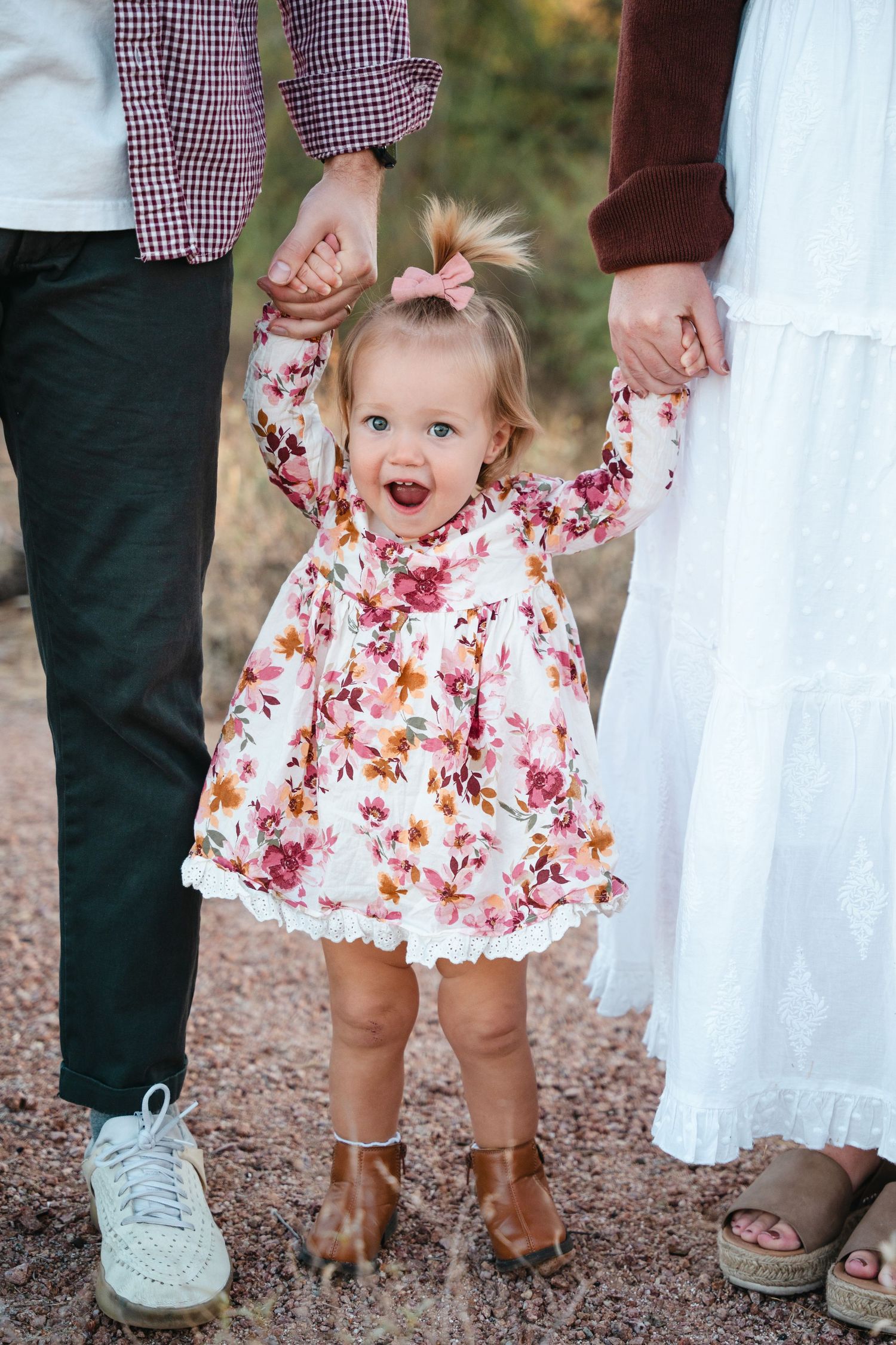 Des Moines Iowa family photographer – joyful parents and toddler girl holding hands raised high, smiling together outdoors in natural light.