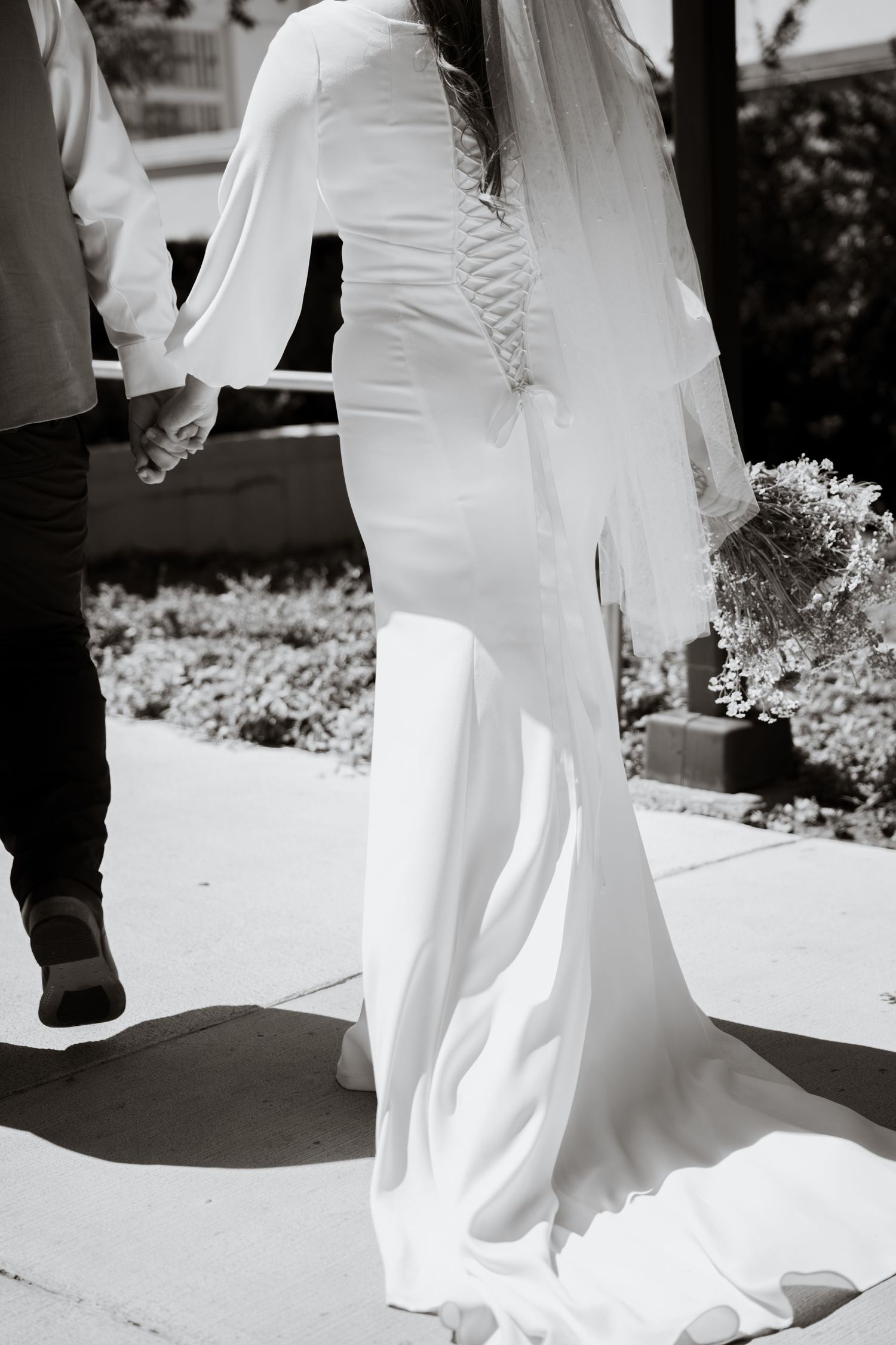 Bridal couple holding hands on wedding day walking. Detail shot of the back of the dress on a warm Des Moines day.