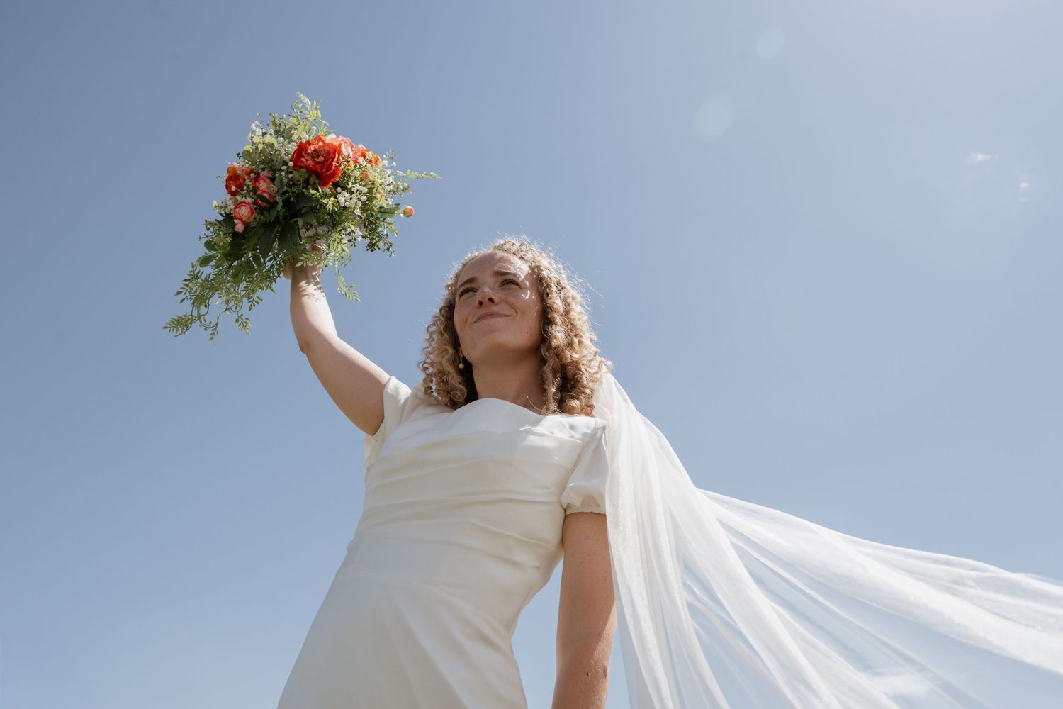 Des Moines wedding photography detail: bride holding up bouquet under summer blue sky.