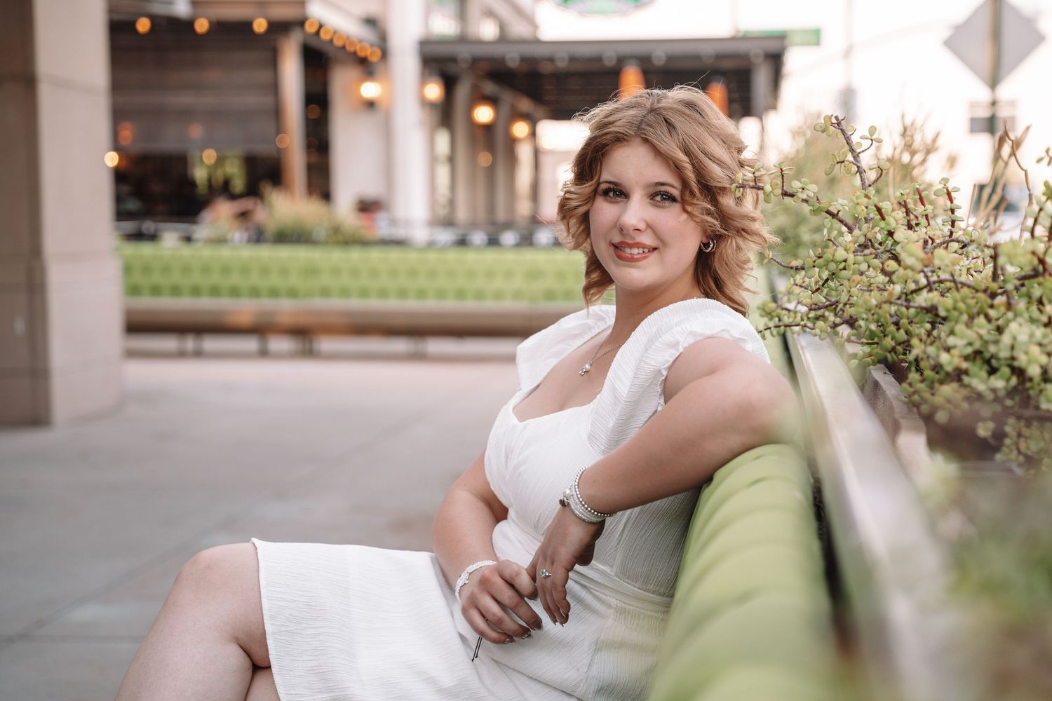 Des Moines Iowa senior portrait photographer – happy teenage girl in white dress sitting outdoors, warm smile and relaxed pose.